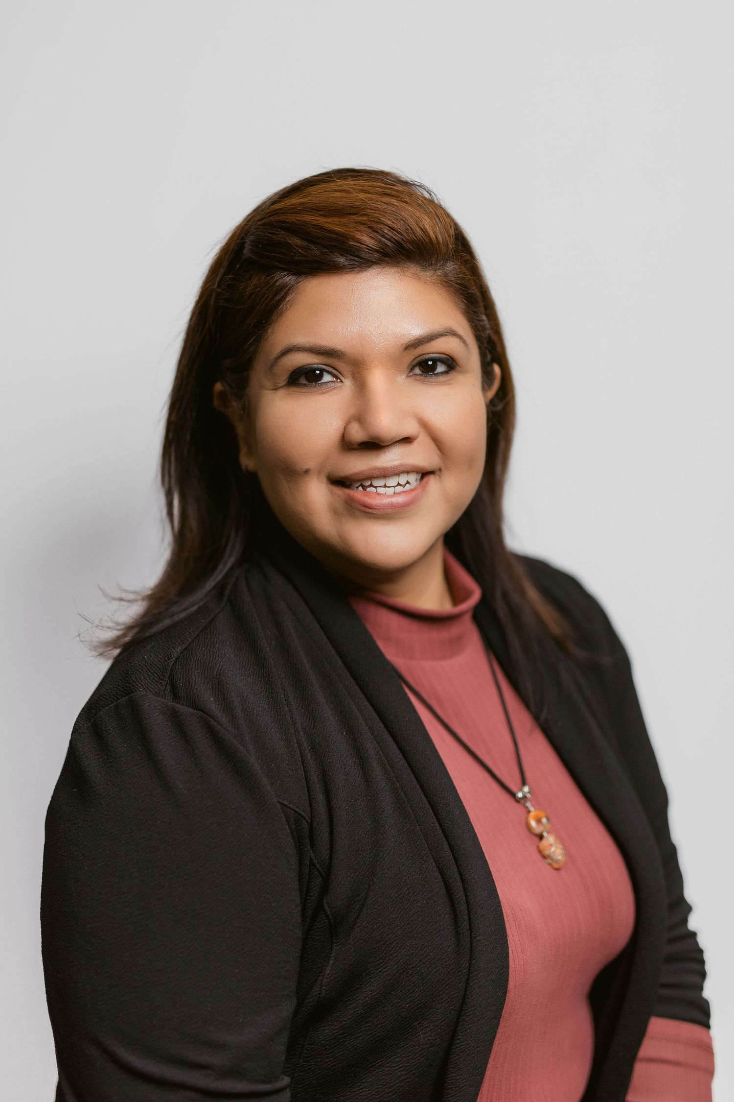 Professional headshots of person wearing black blazer and coral top against white background.