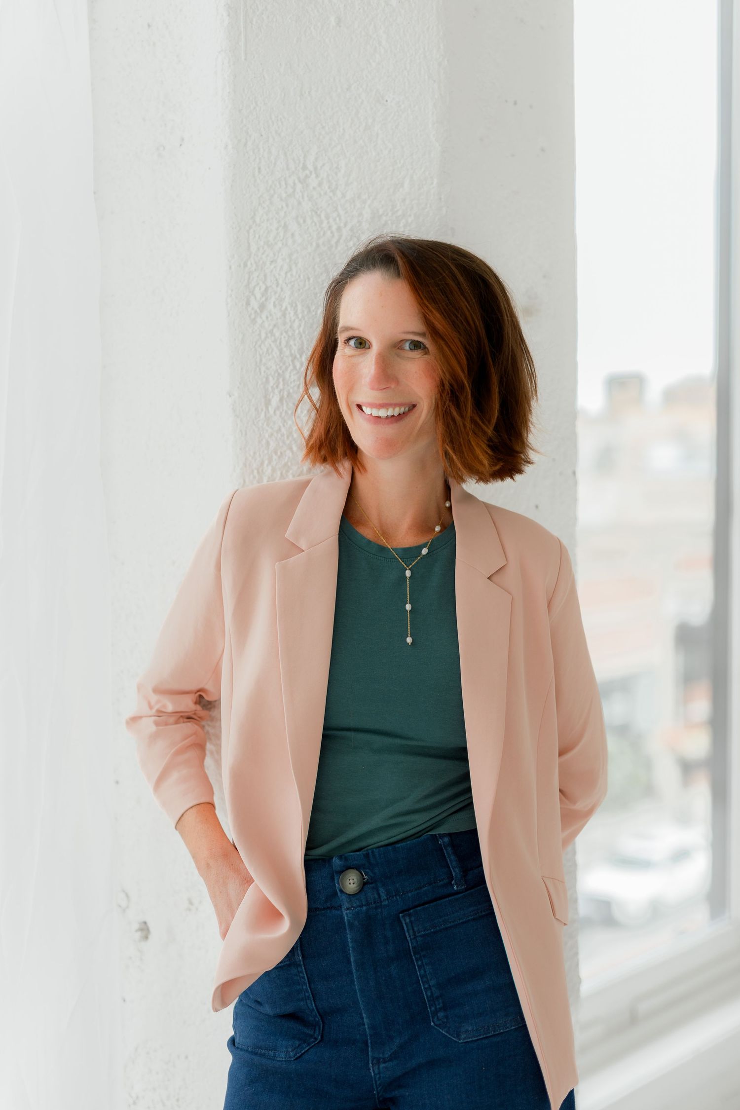 Stylish portrait in pink blazer and green top against bright window background.