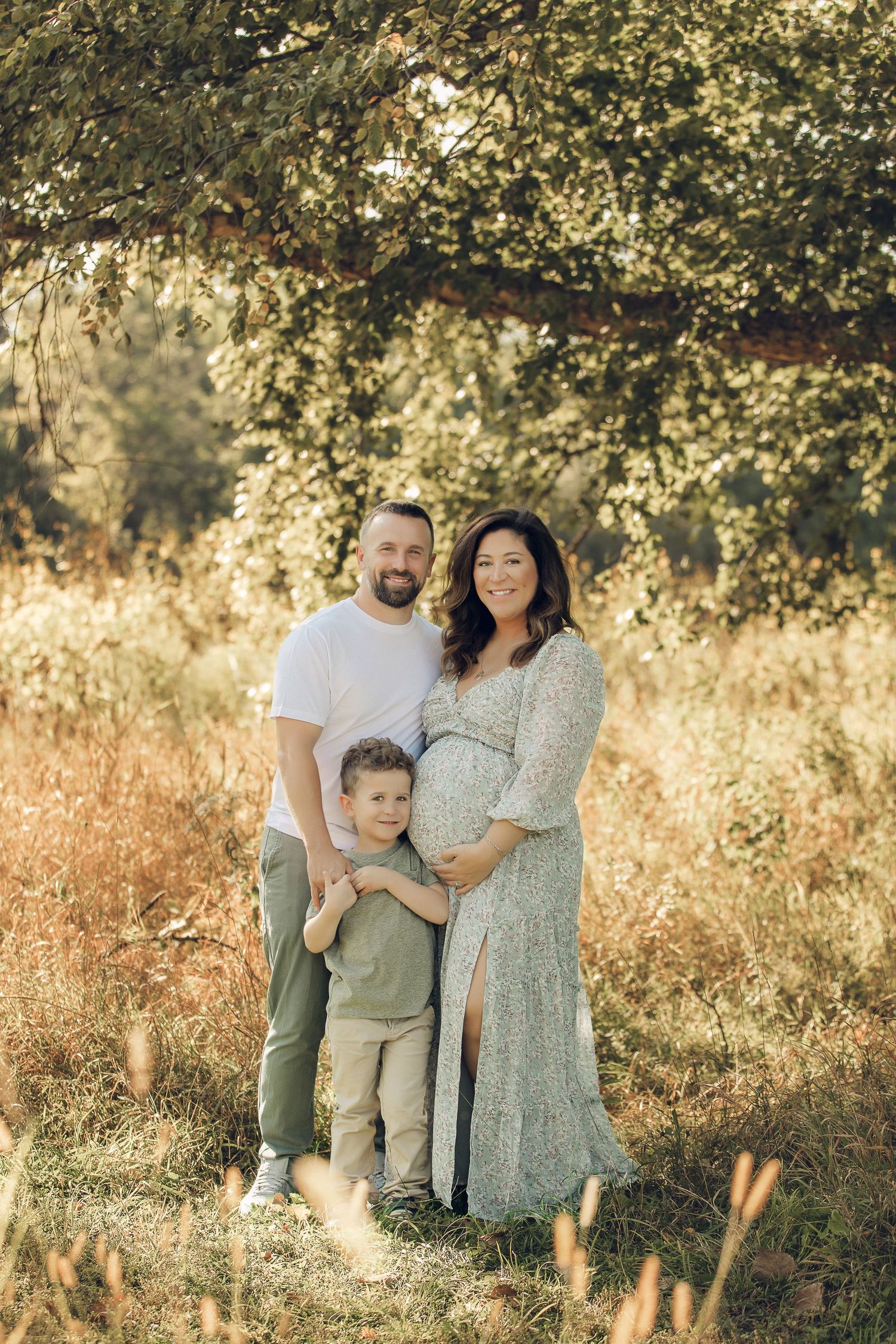 Family portrait beneath tree branches in golden afternoon light.