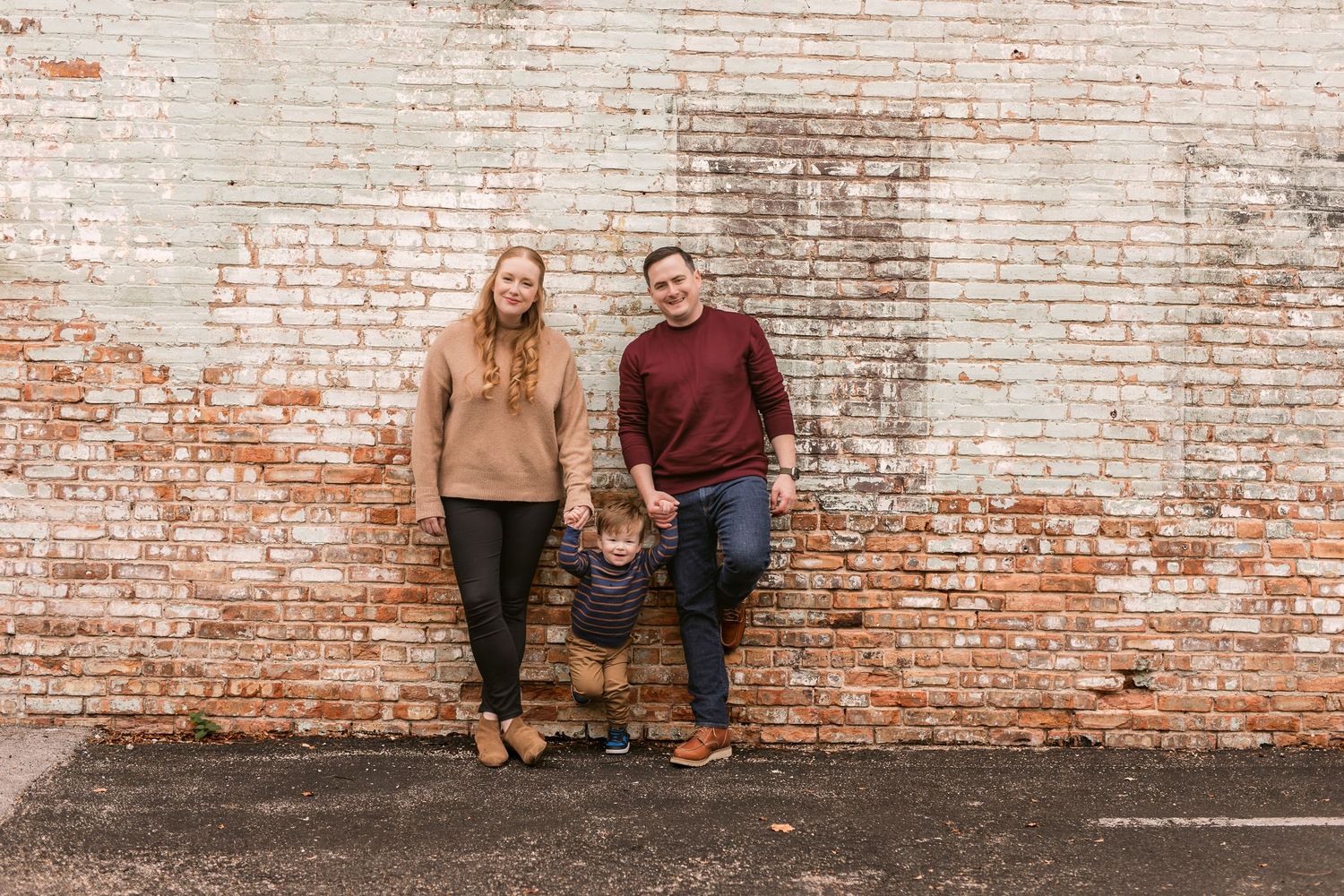 A couple poses against a rustic brick wall for engagement photos in a series of candid shots.