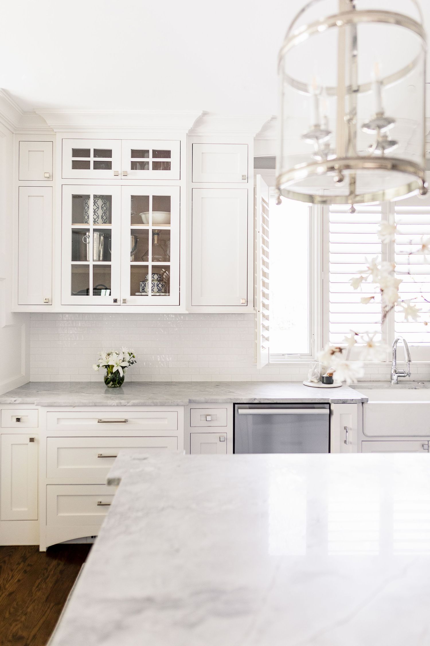 Modern white kitchen with glass pendant lights, white cabinets, and marble countertops features a bright airy design.