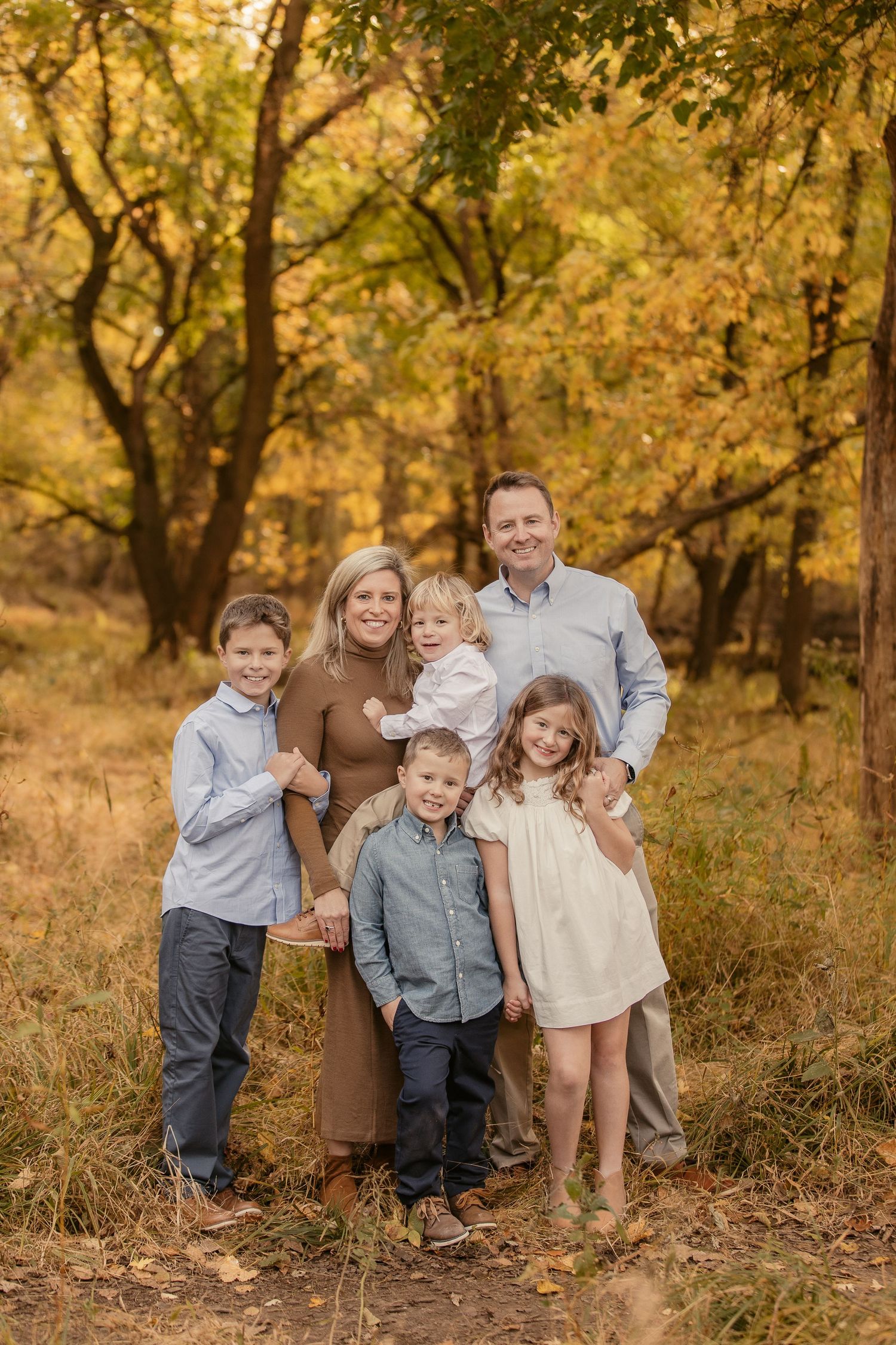 A family portrait captured in a warm autumn forest setting with golden leaves.