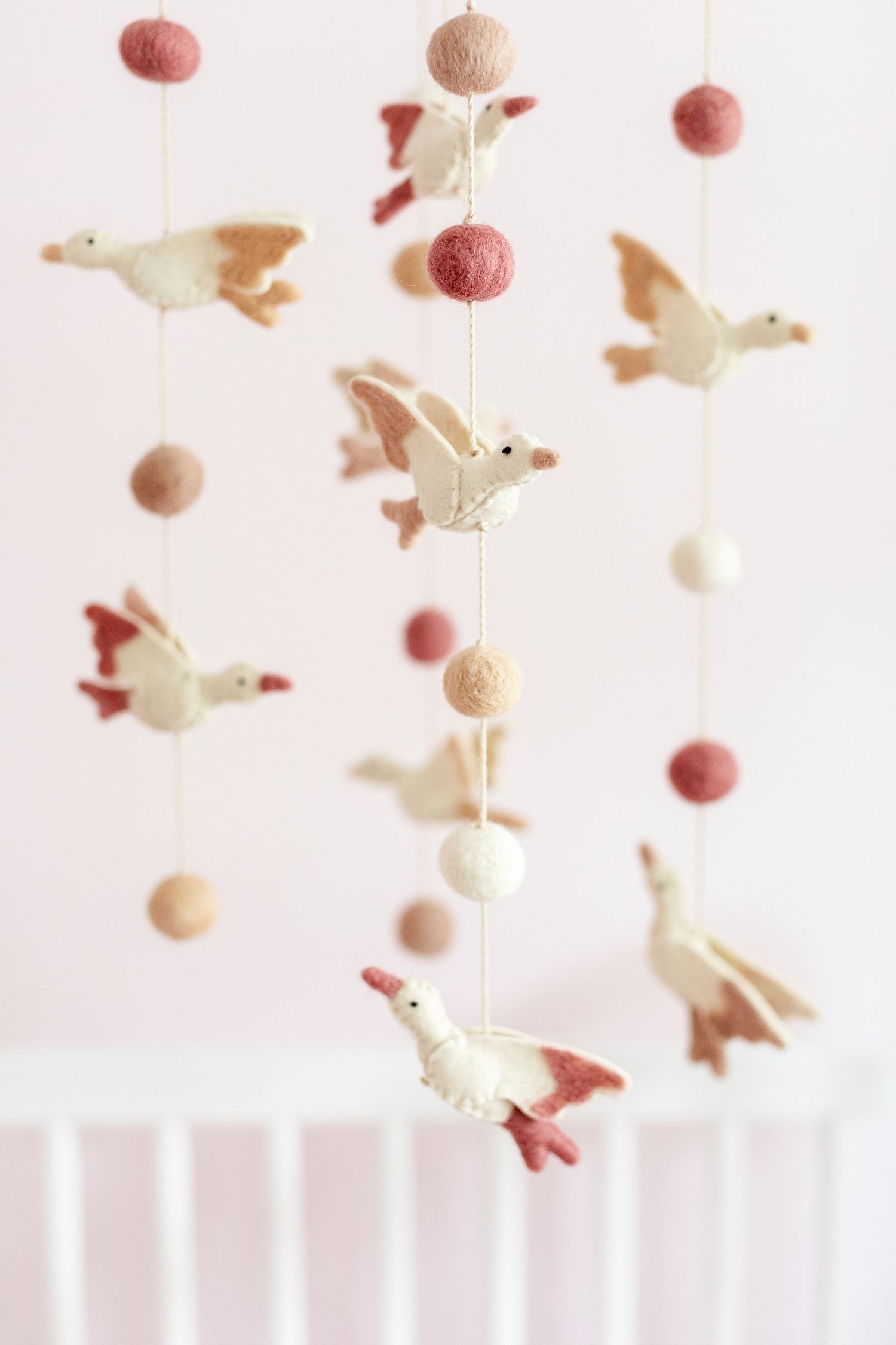 Whimsical mobile with pink pom poms and white birds hanging delicately against a light background.