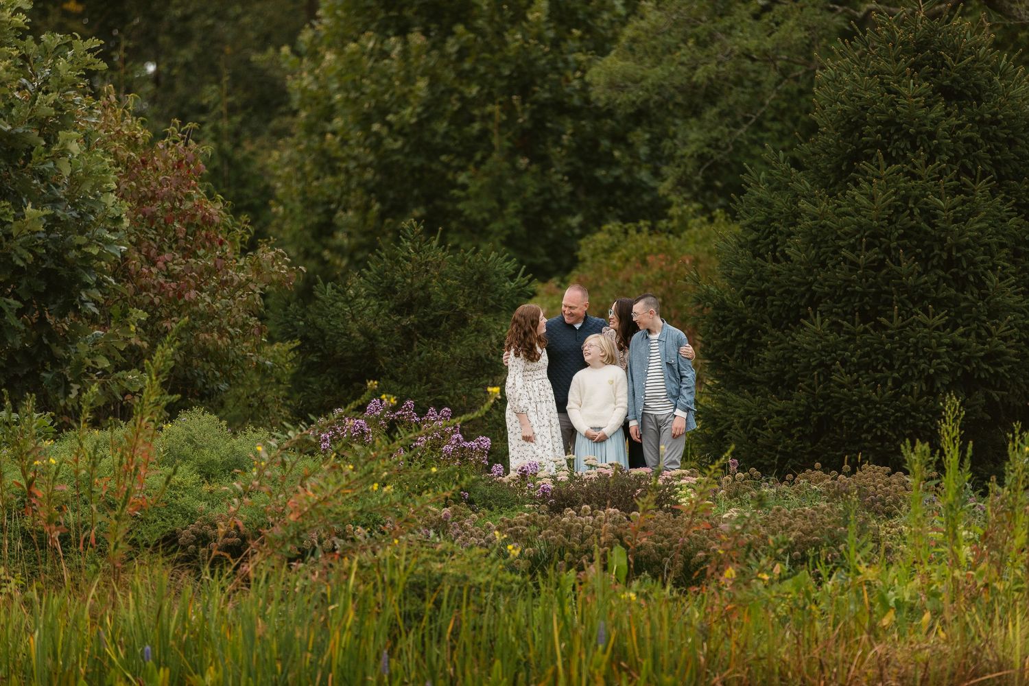 Family of four gathered among wildflowers and lush greenery in a scenic outdoor garden setting.