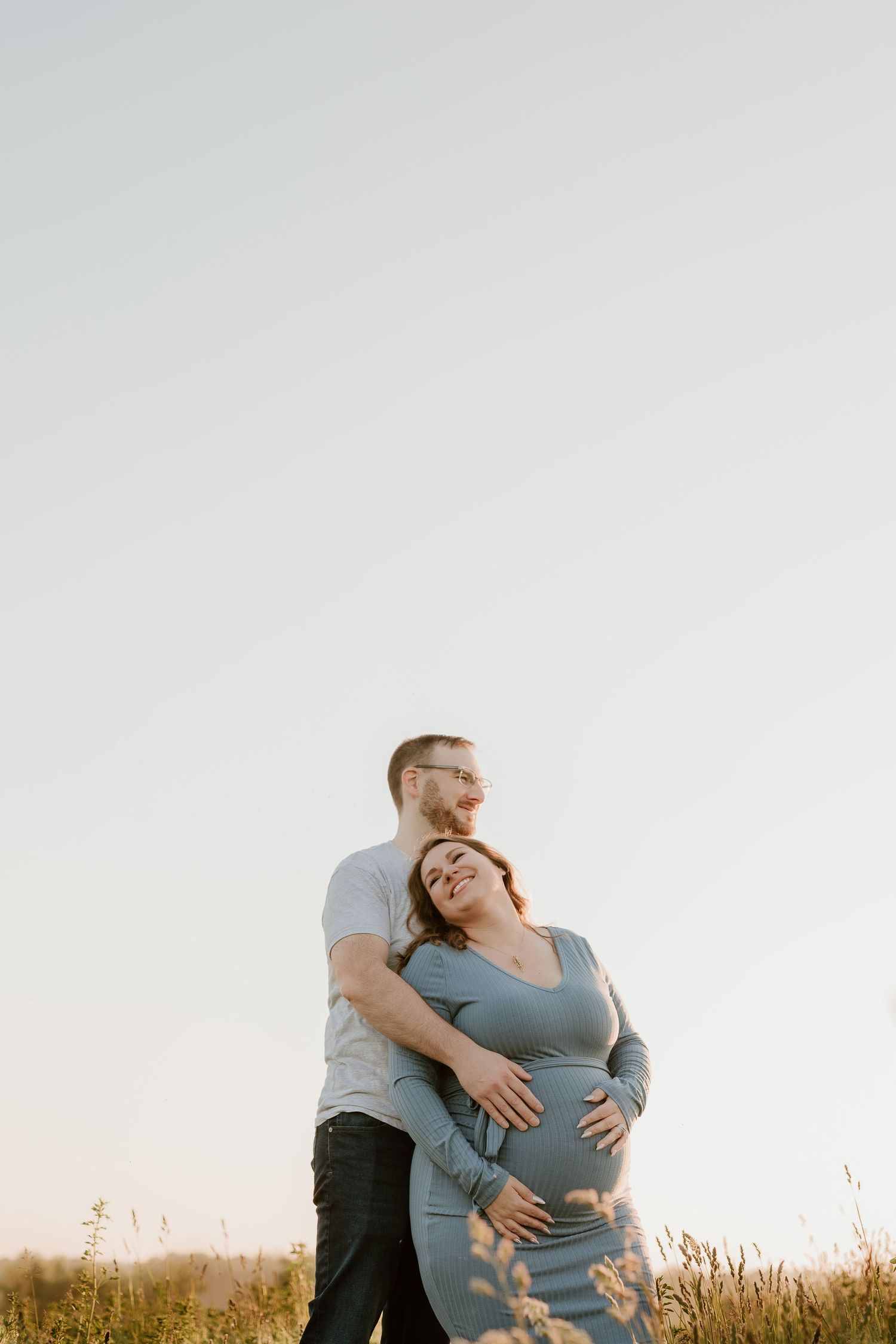A couple embraces during sunset in a grassy field during a maternity photoshoot.