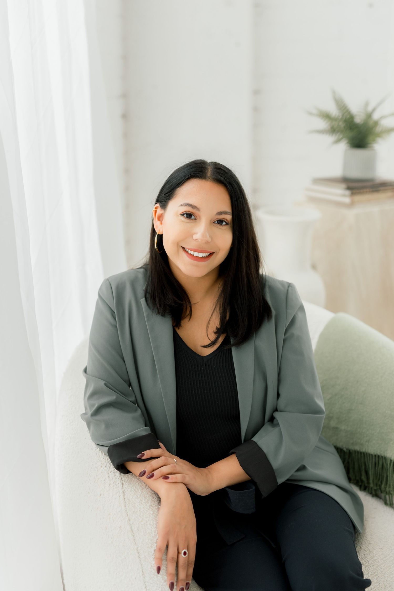 Professional in gray blazer and black top poses in modern studio setting.