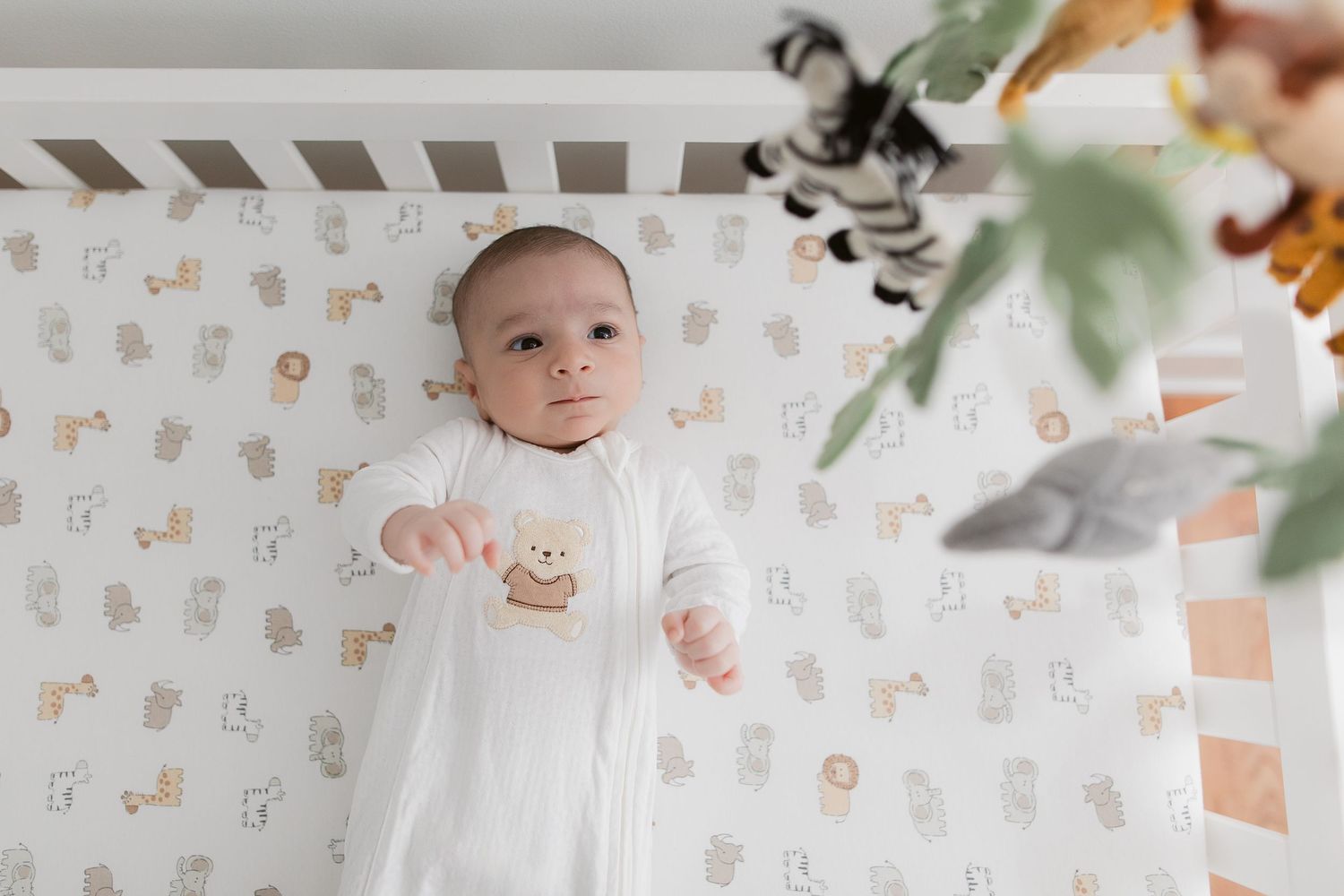 Infant resting on patterned blanket with delicate animal print and green foliage accents.