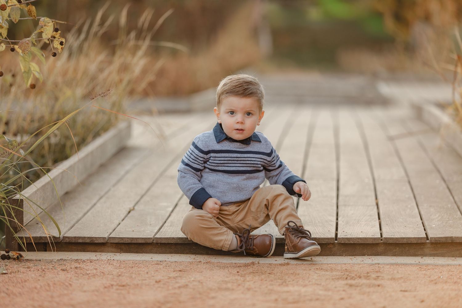Young child sitting and playing on wooden boardwalk during outdoor photo session.