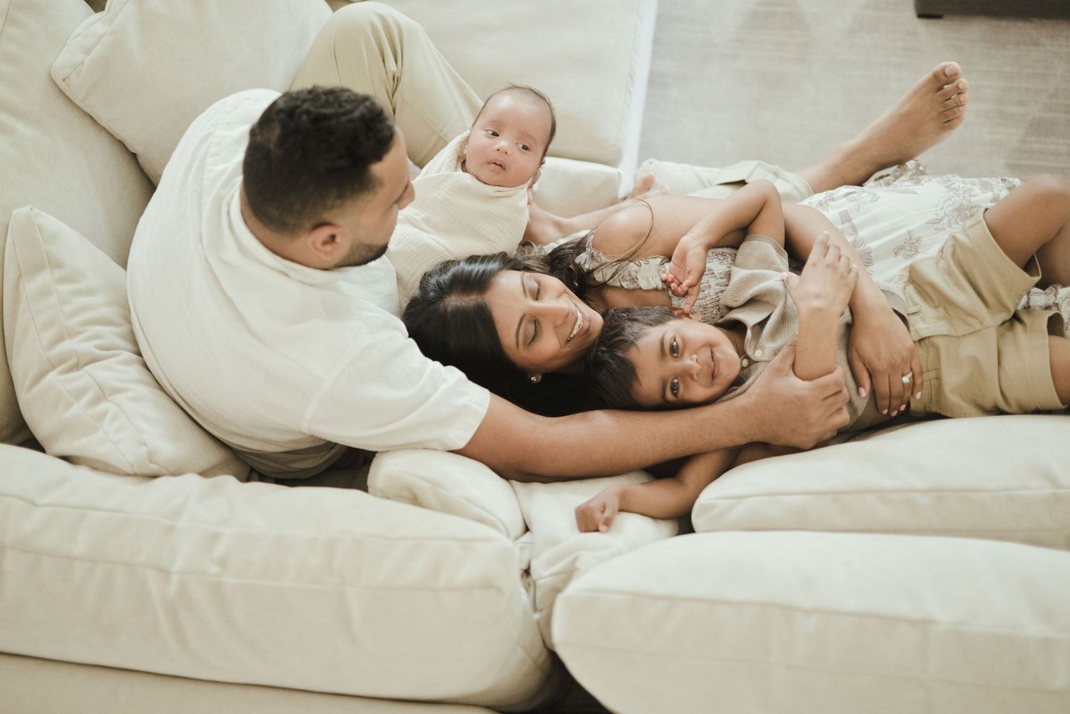 A happy family with two young children relaxing together on a cozy white sofa at home.