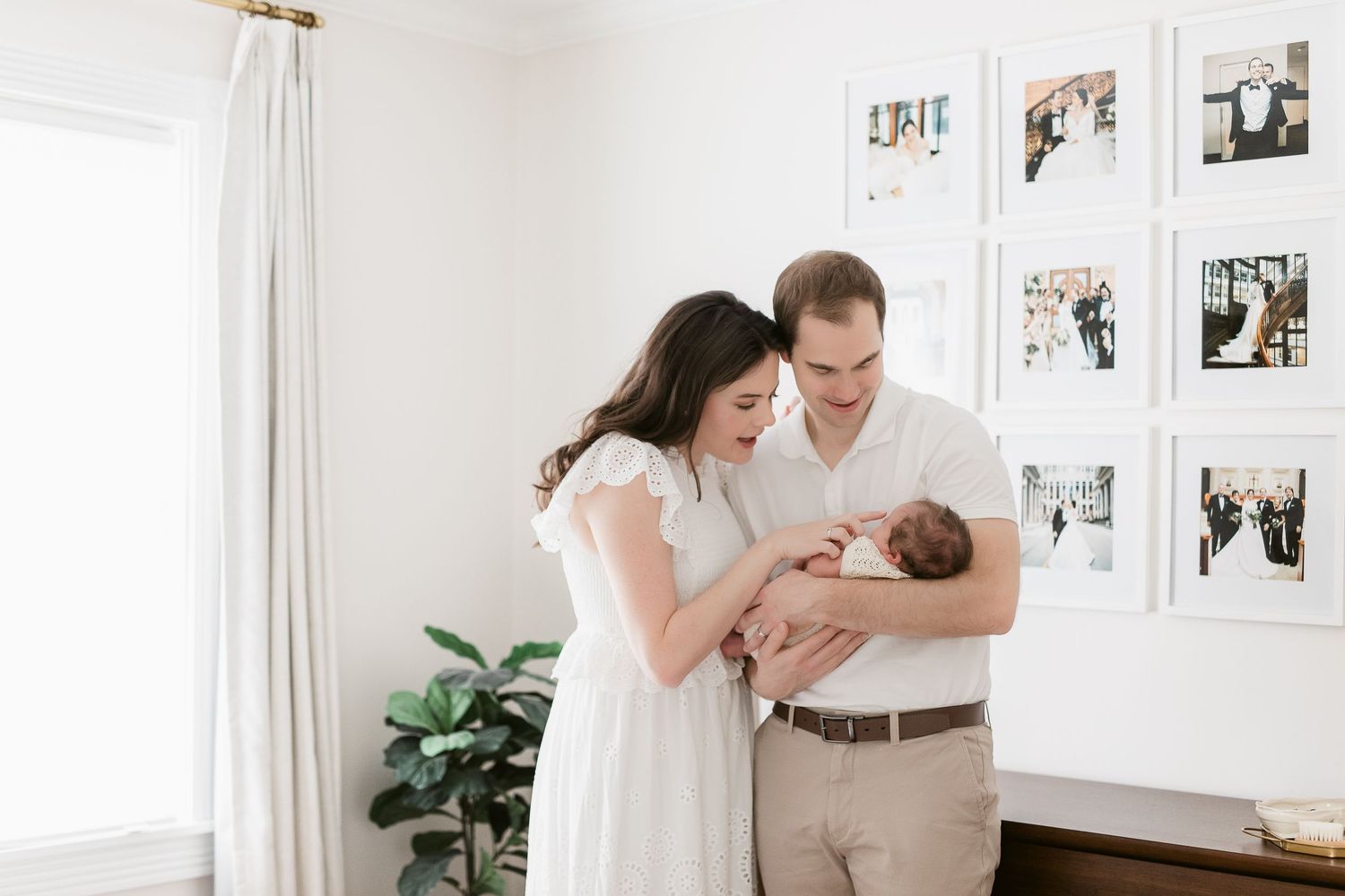 Family portrait session in bright white room with framed photos on wall.