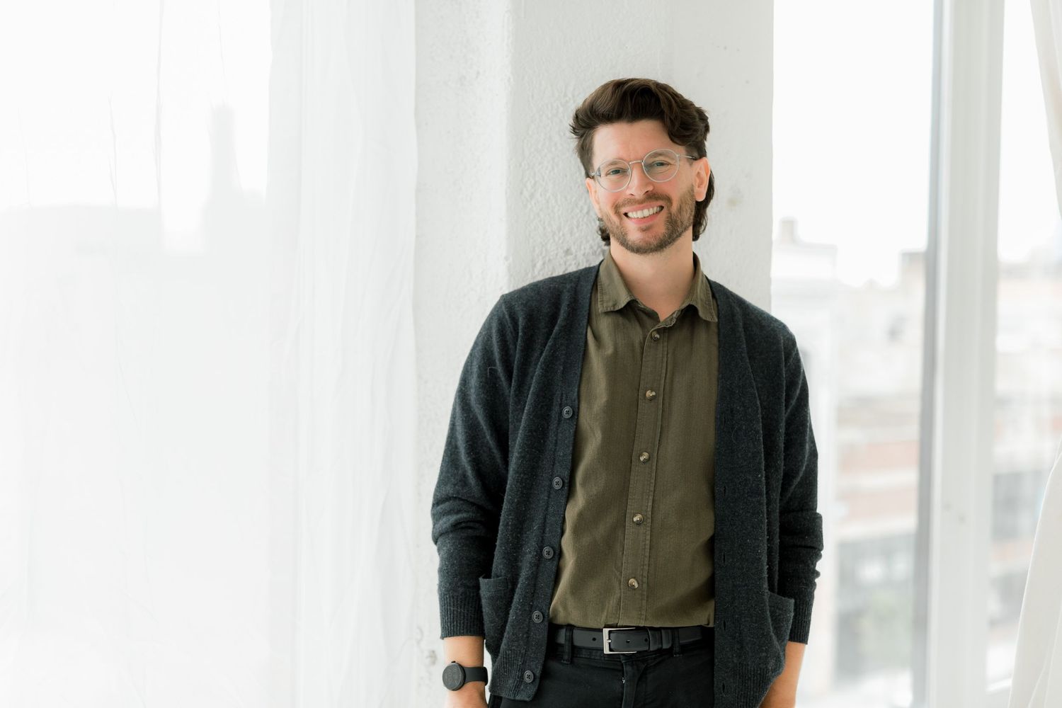 Casual business portrait by window wearing dark cardigan and olive button-up shirt.