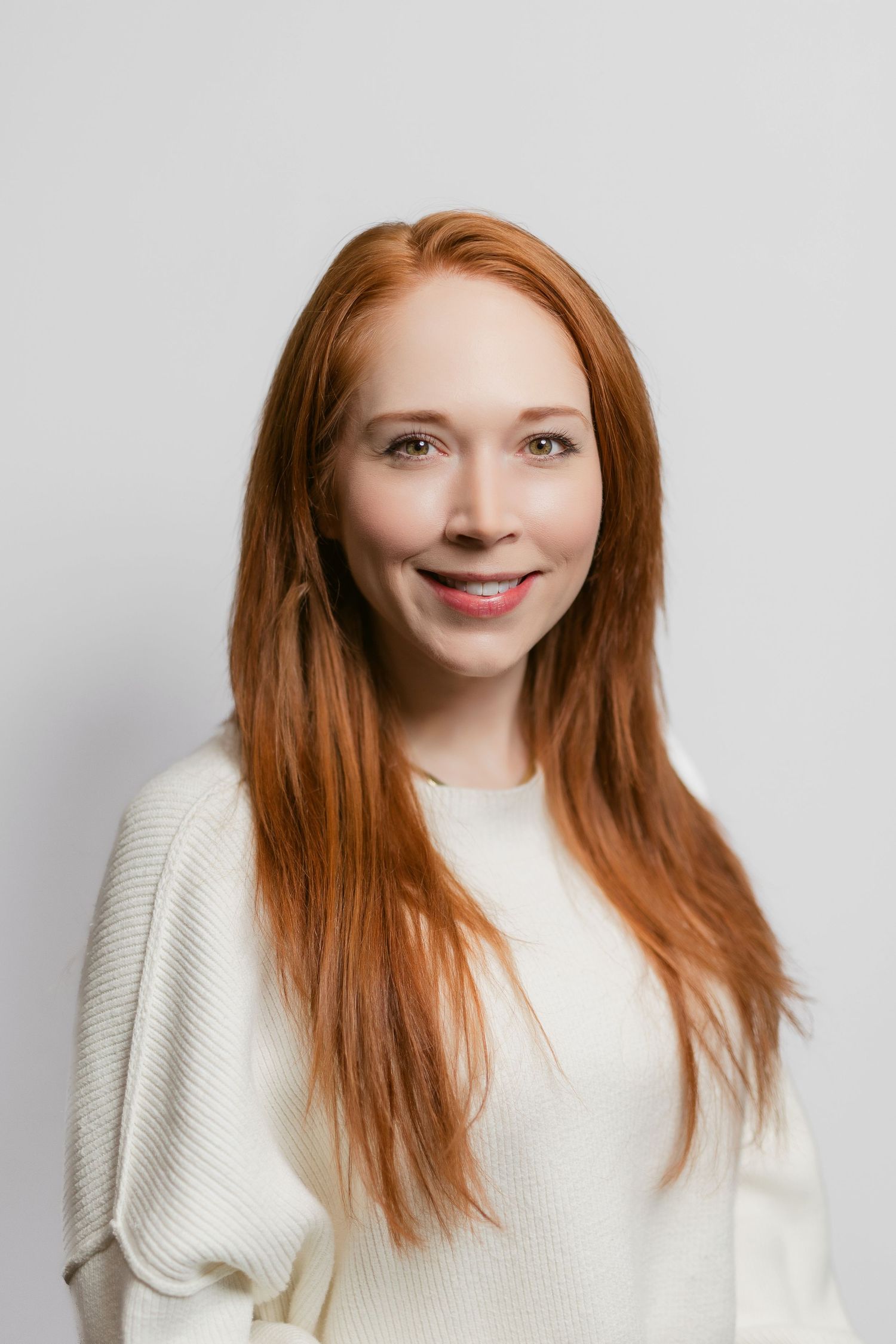 Professional portraits of person with long red hair wearing cream sweater against white background.