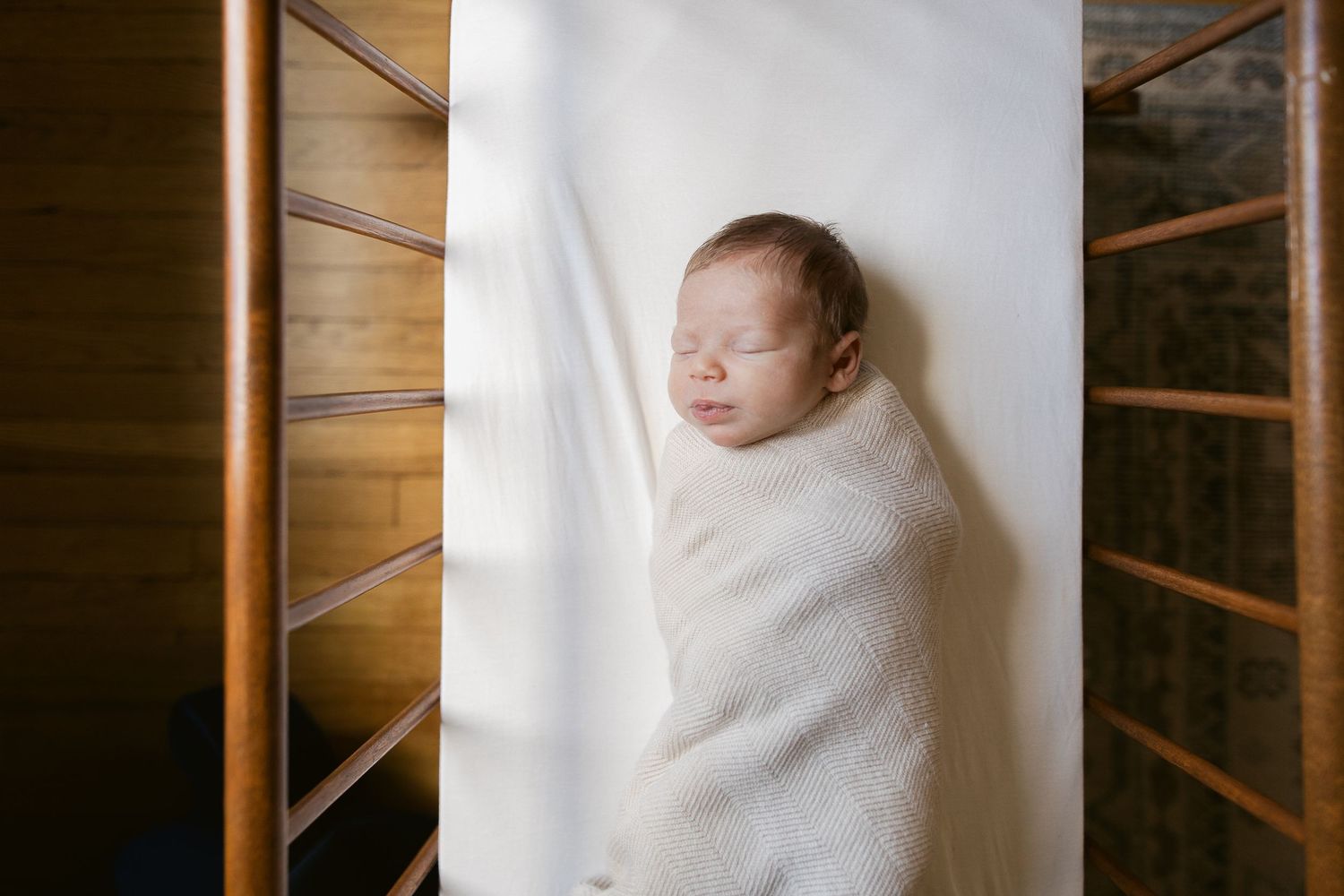 Peaceful sleeping newborn wrapped in white blanket against wooden background.