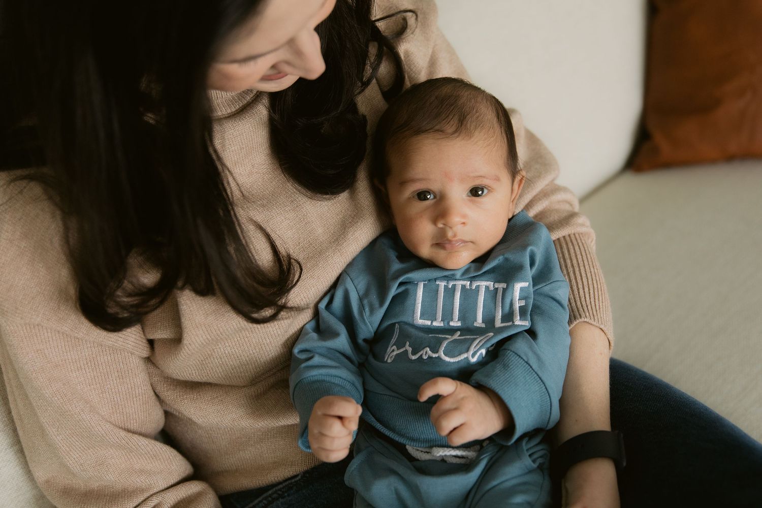 A baby in a blue shirt sits on someone's lap while playing and interacting in a warmly lit room.