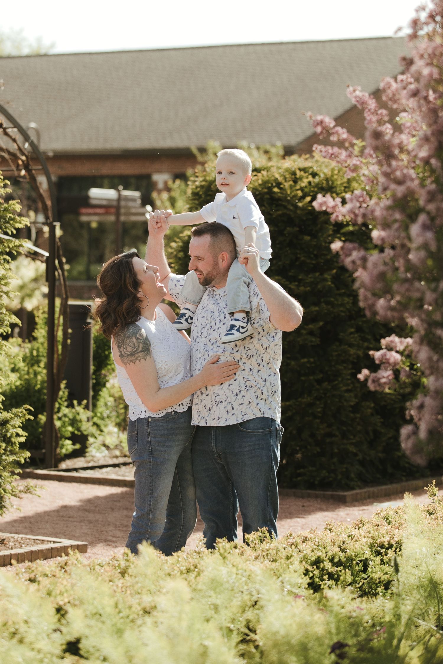 A happy family poses in a blooming garden, with a father lifting a baby while a mother smiles nearby.