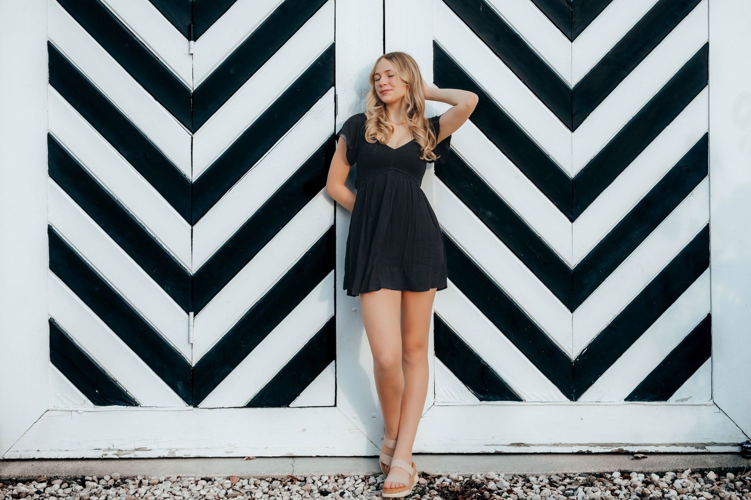 A person in a black dress poses in front of a bold black and white chevron patterned wall.