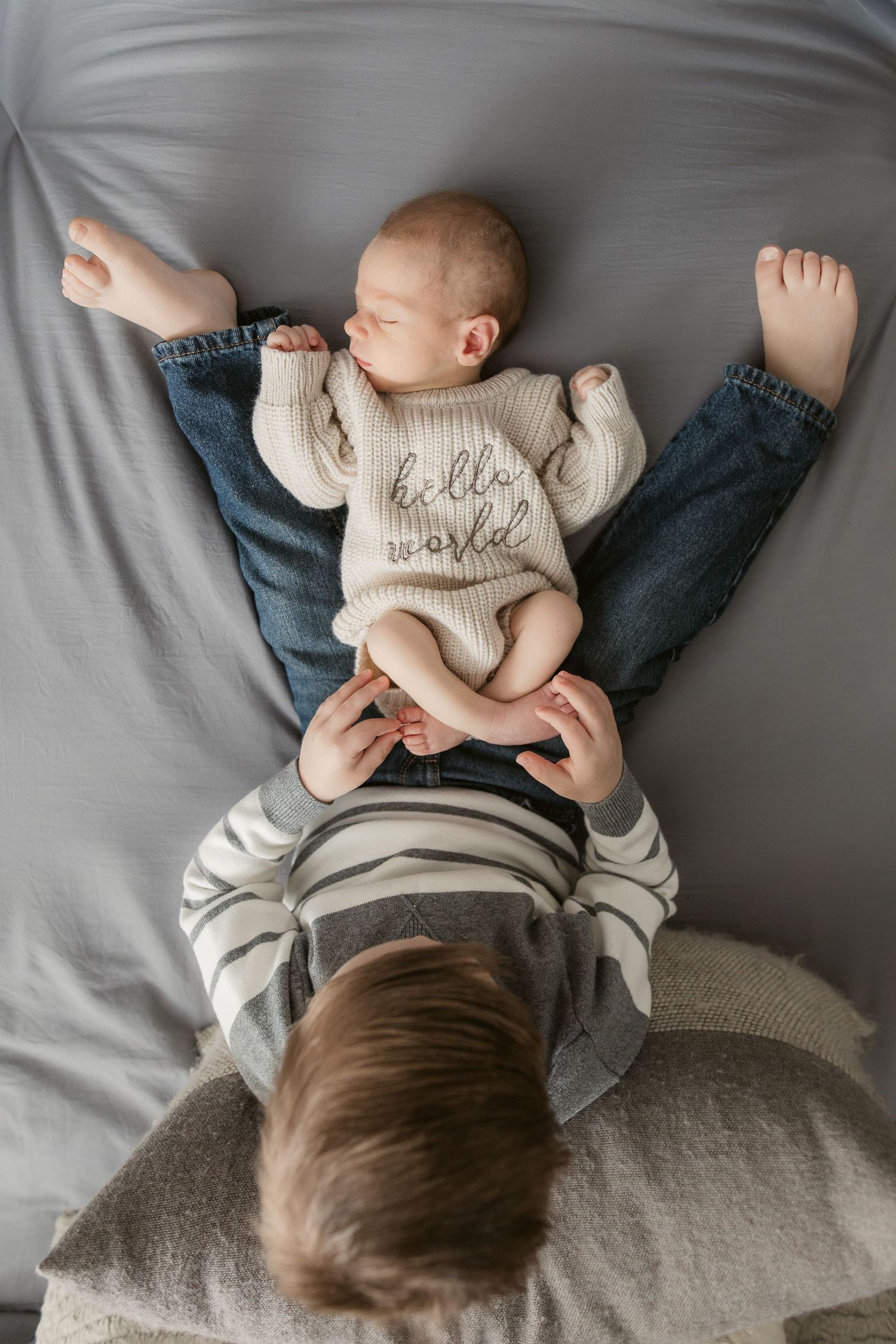 Two siblings sharing sweet moment on grey bedding.