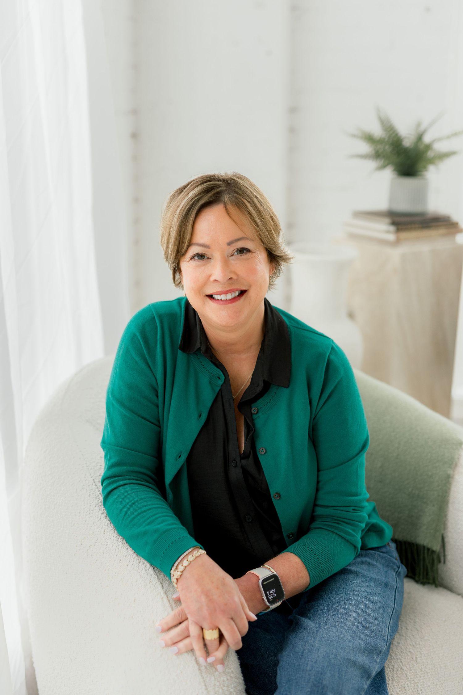 Casual professional photos of a person in green blazer and jeans sitting on light colored furniture.