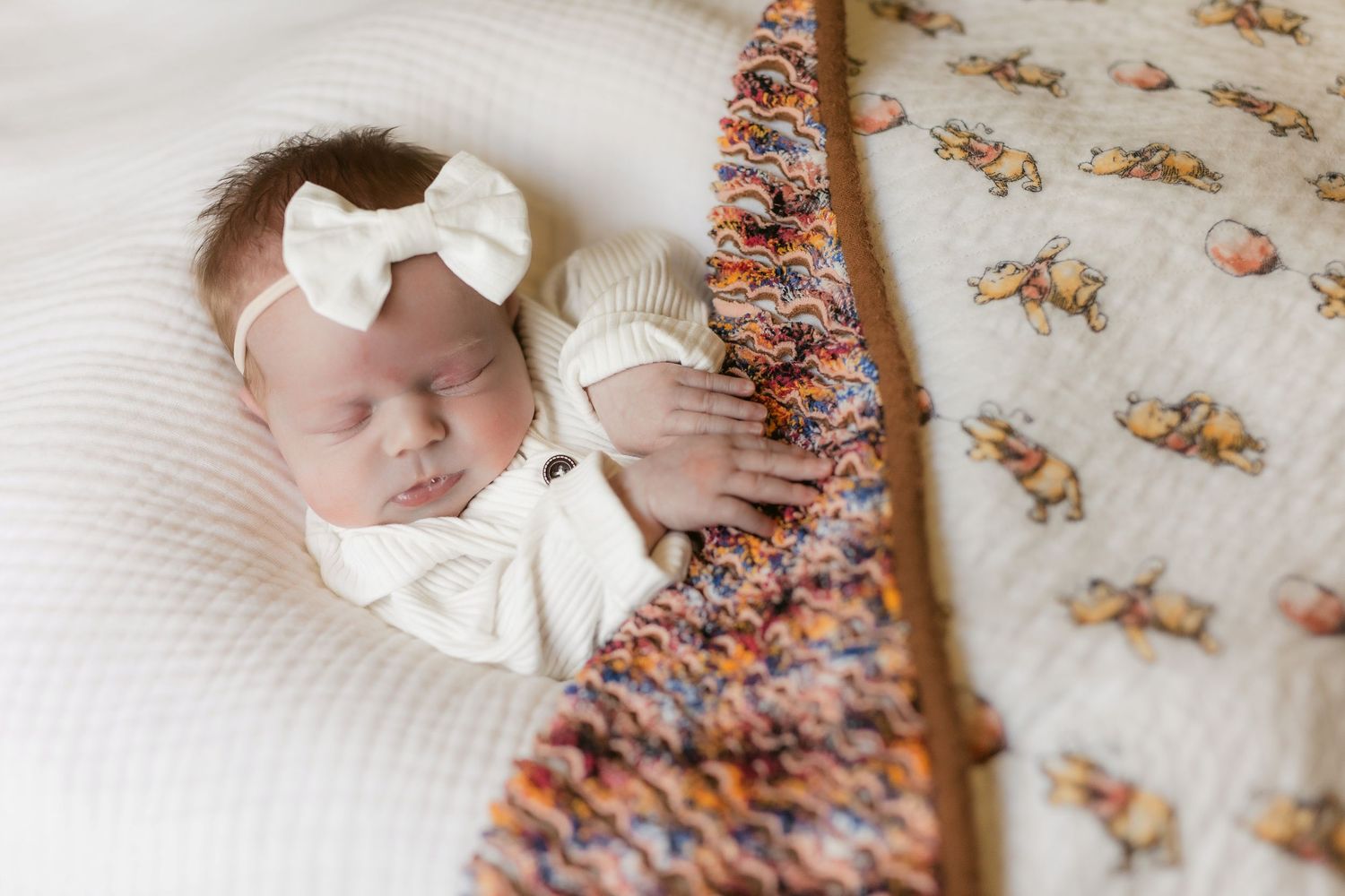 A sleeping baby lies on floral patterned bedding wearing a white bow.