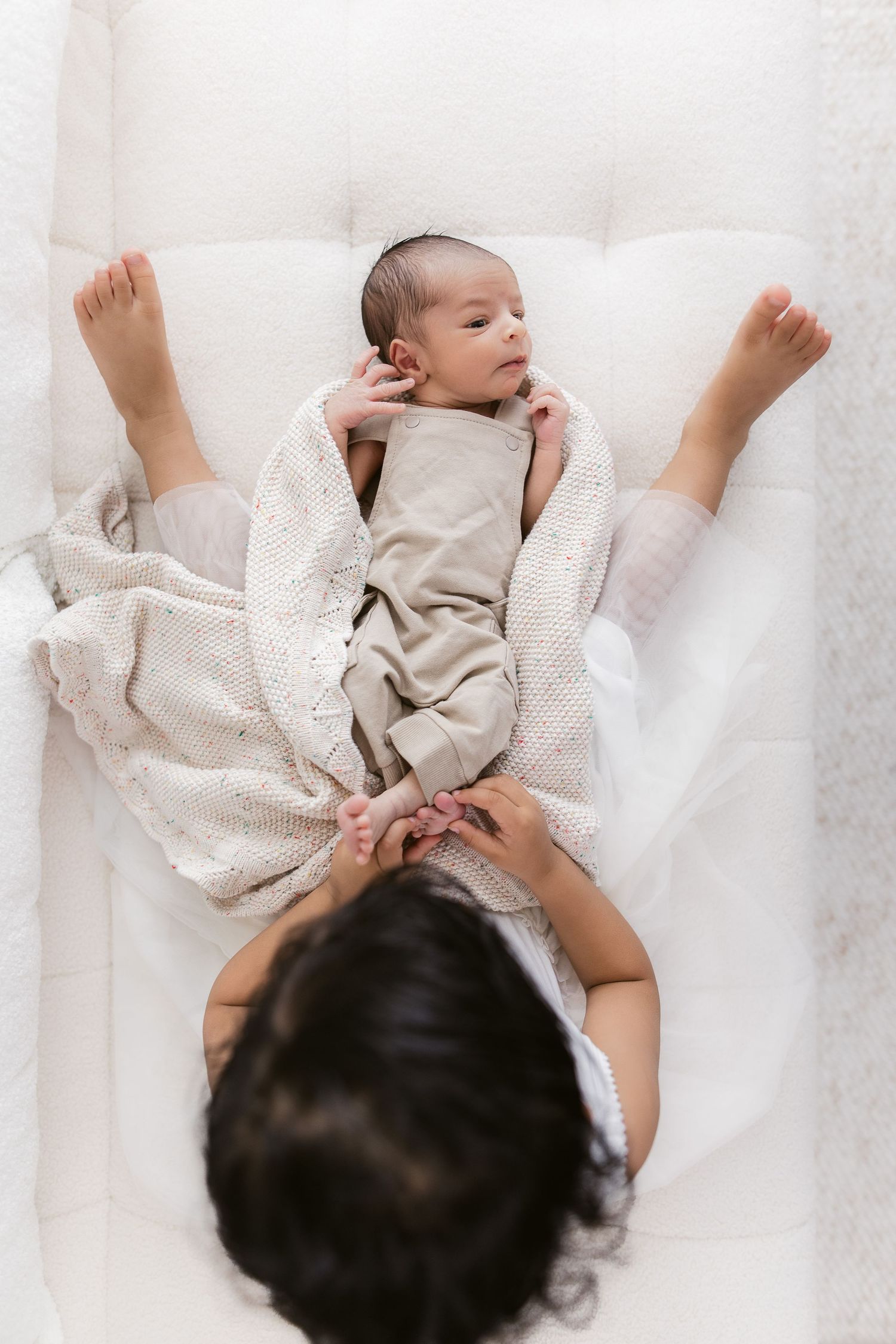 Overhead view of newborn baby lying on white blanket during photoshoot.