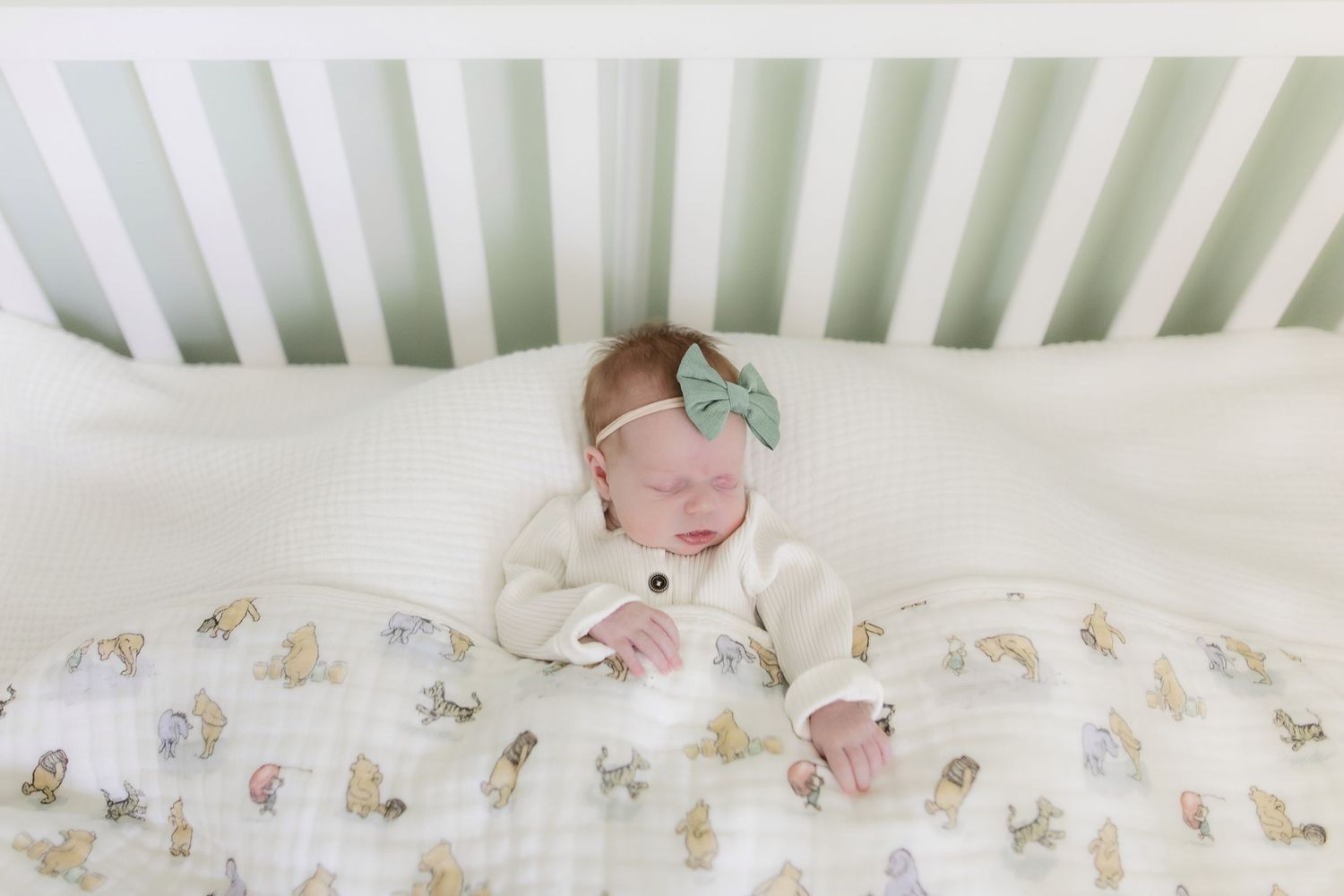 View from above of a baby sleeping in a white crib with patterned sheets.
