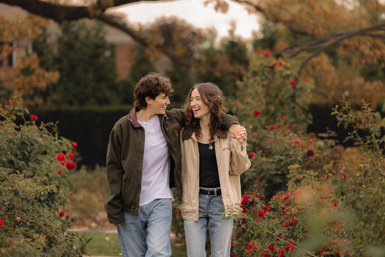 Couple walking through garden path with blooming red roses and fall foliage.