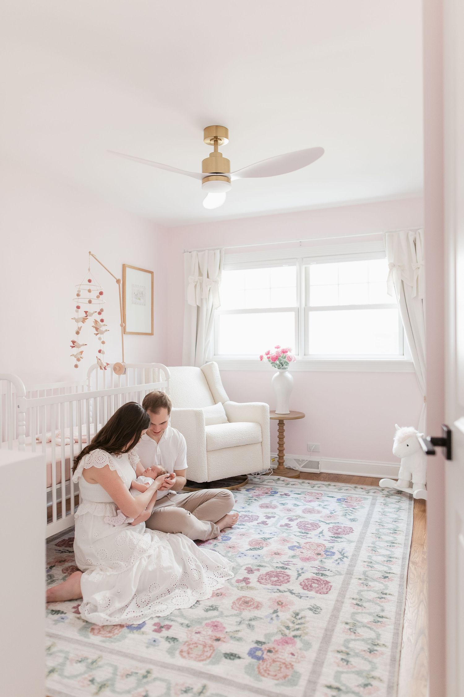 Family bonding on a floral bedspread in a light-filled bedroom with white decor.