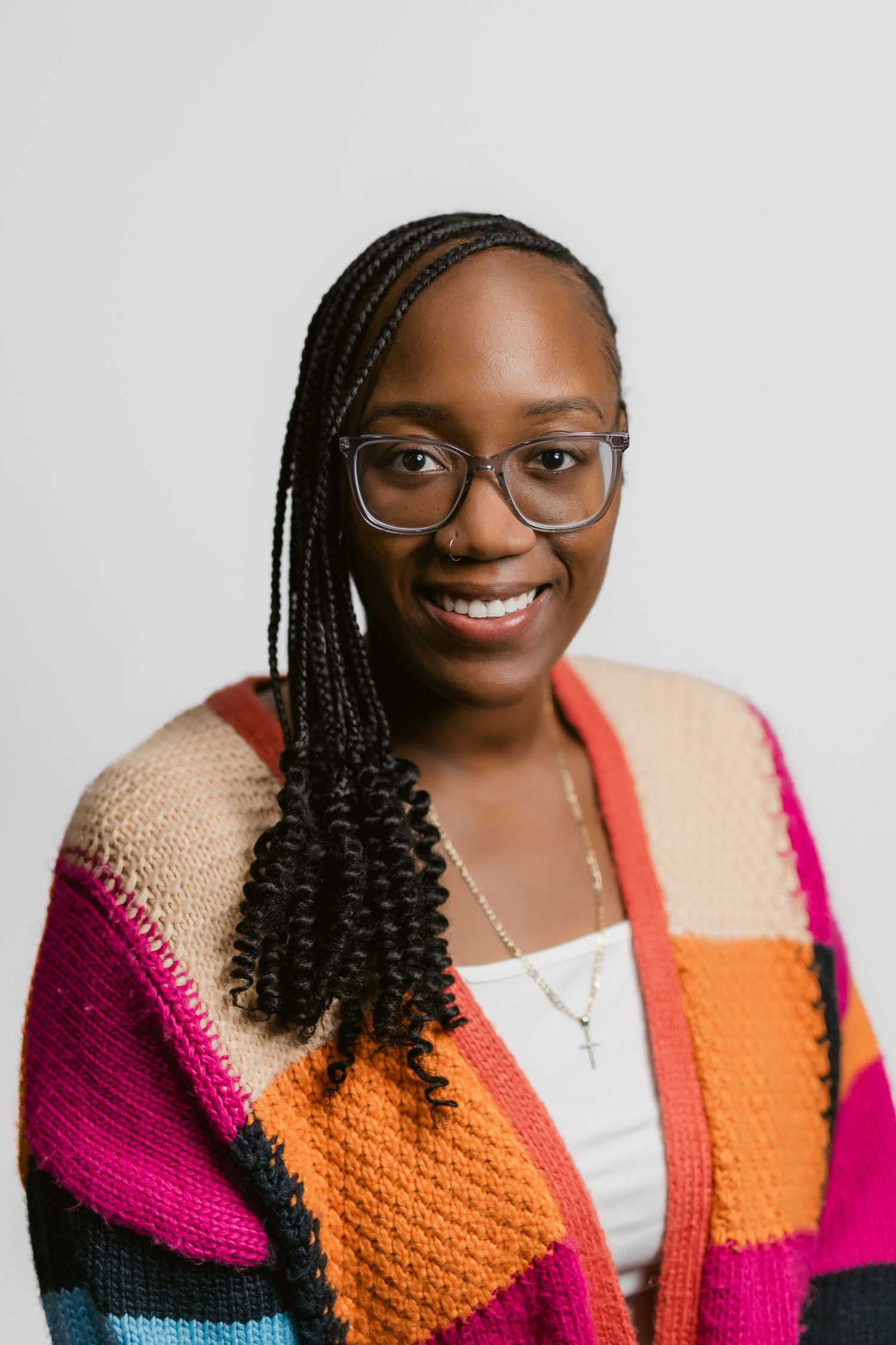 Professional portraits of person in colorful knit cardigan with braided hair against light background.