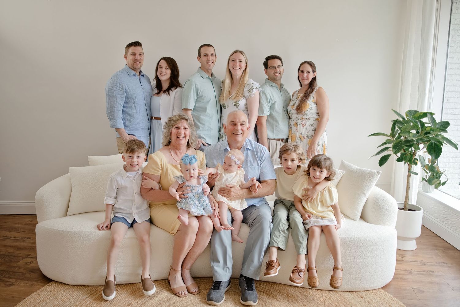 Large multigenerational family portrait with grandparents, parents, and children posing together on a white sofa.