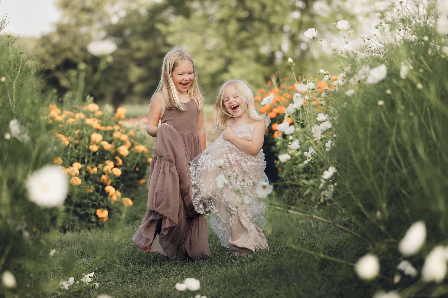 Two figures in flowing dresses dance joyfully among yellow and white wildflowers in a sunlit garden.