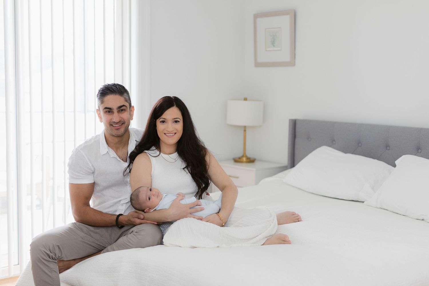 Family relaxing together on white bedding in bright, minimalist bedroom.