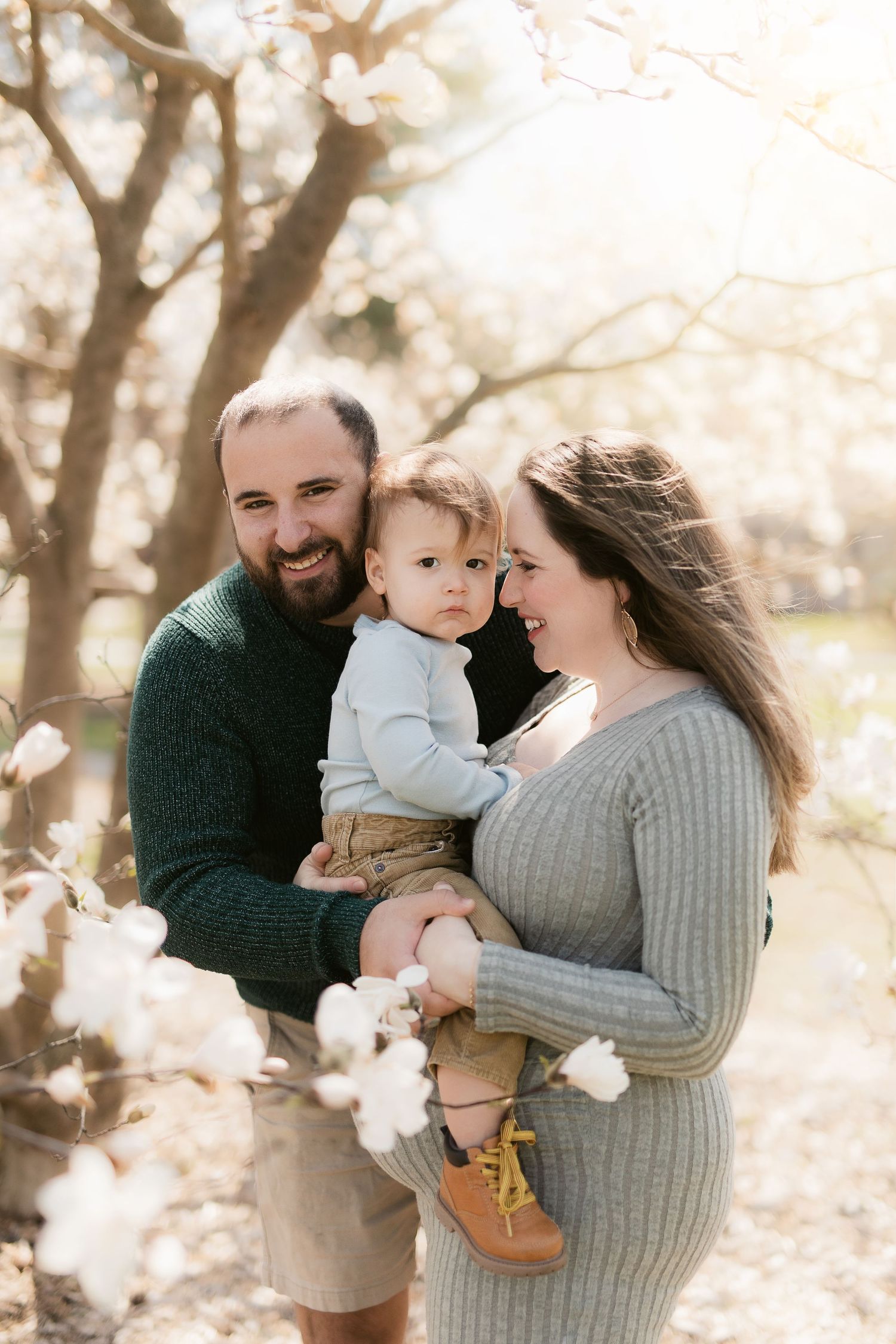 Family enjoying a tender moment together outdoors on a sunny day with blossoming trees in the background.