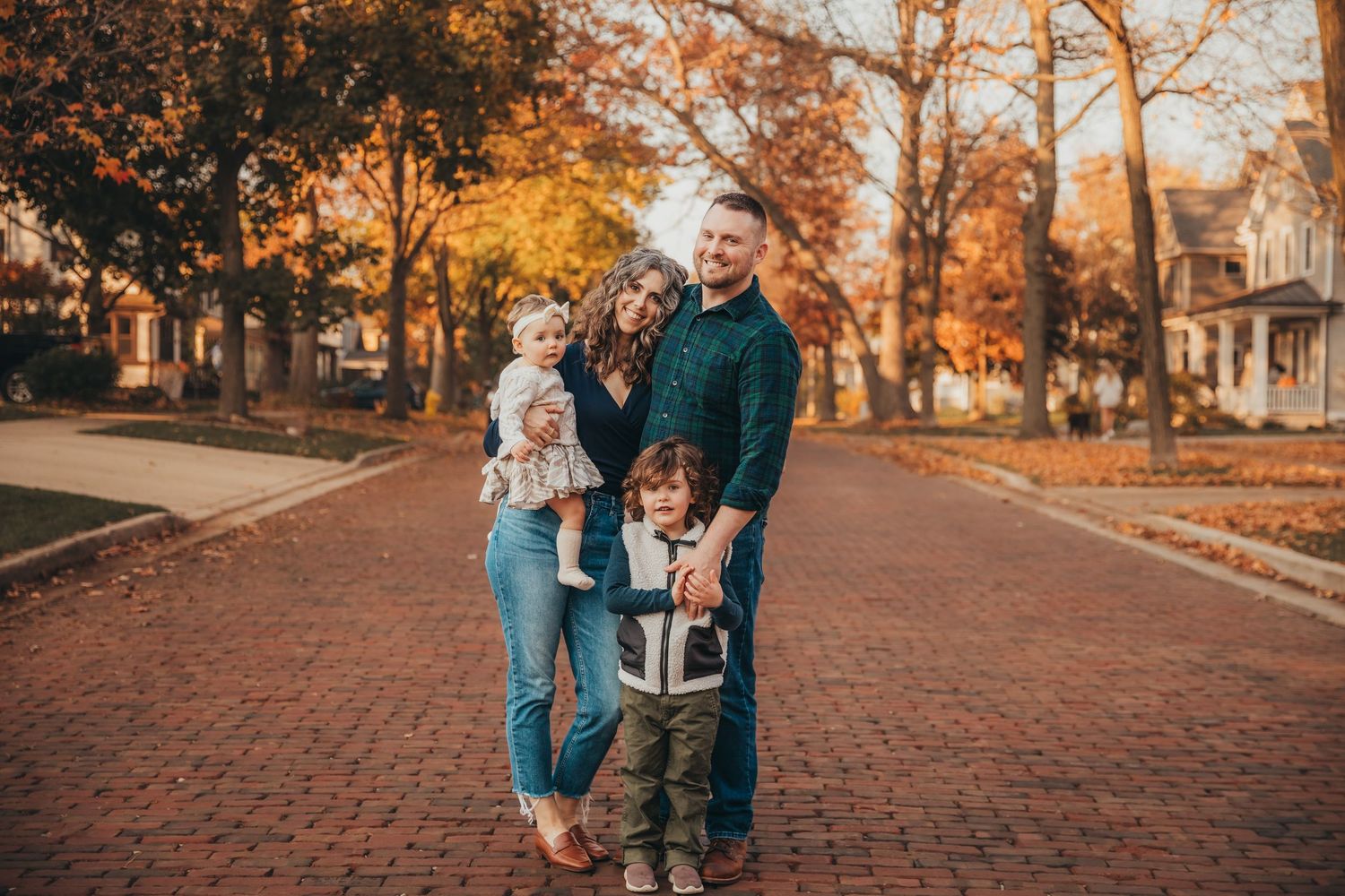 Family walking together on a brick path surrounded by autumn trees during golden hour sunset.