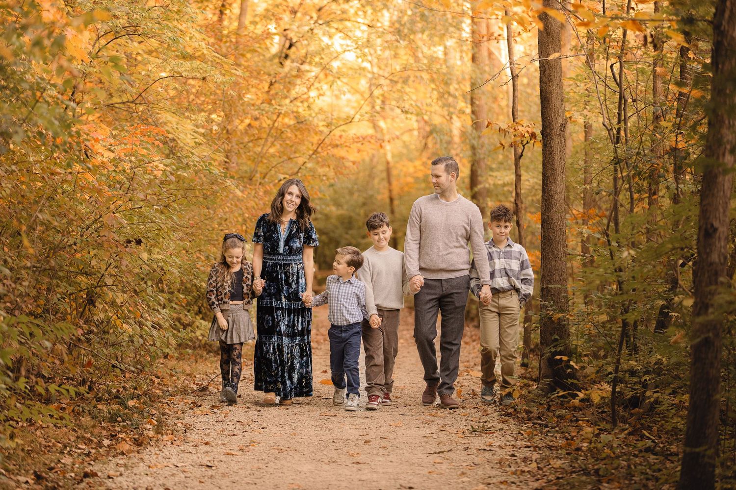 Family of six walking on a autumn forest path surrounded by colorful fall foliage in golden light.