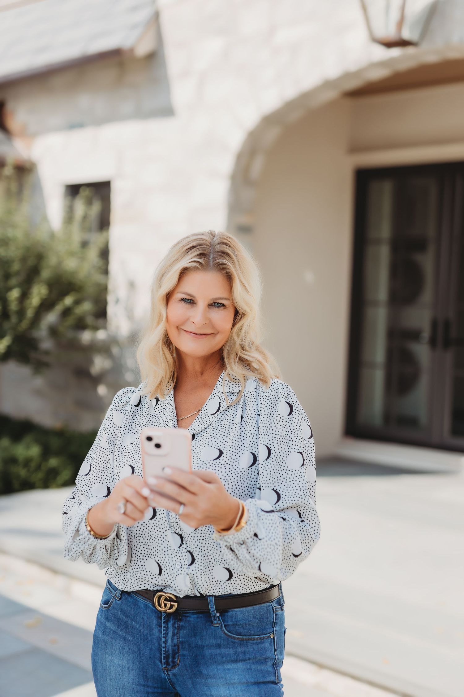 Person wearing a moon phase print top and jeans using a mobile phone outdoors.