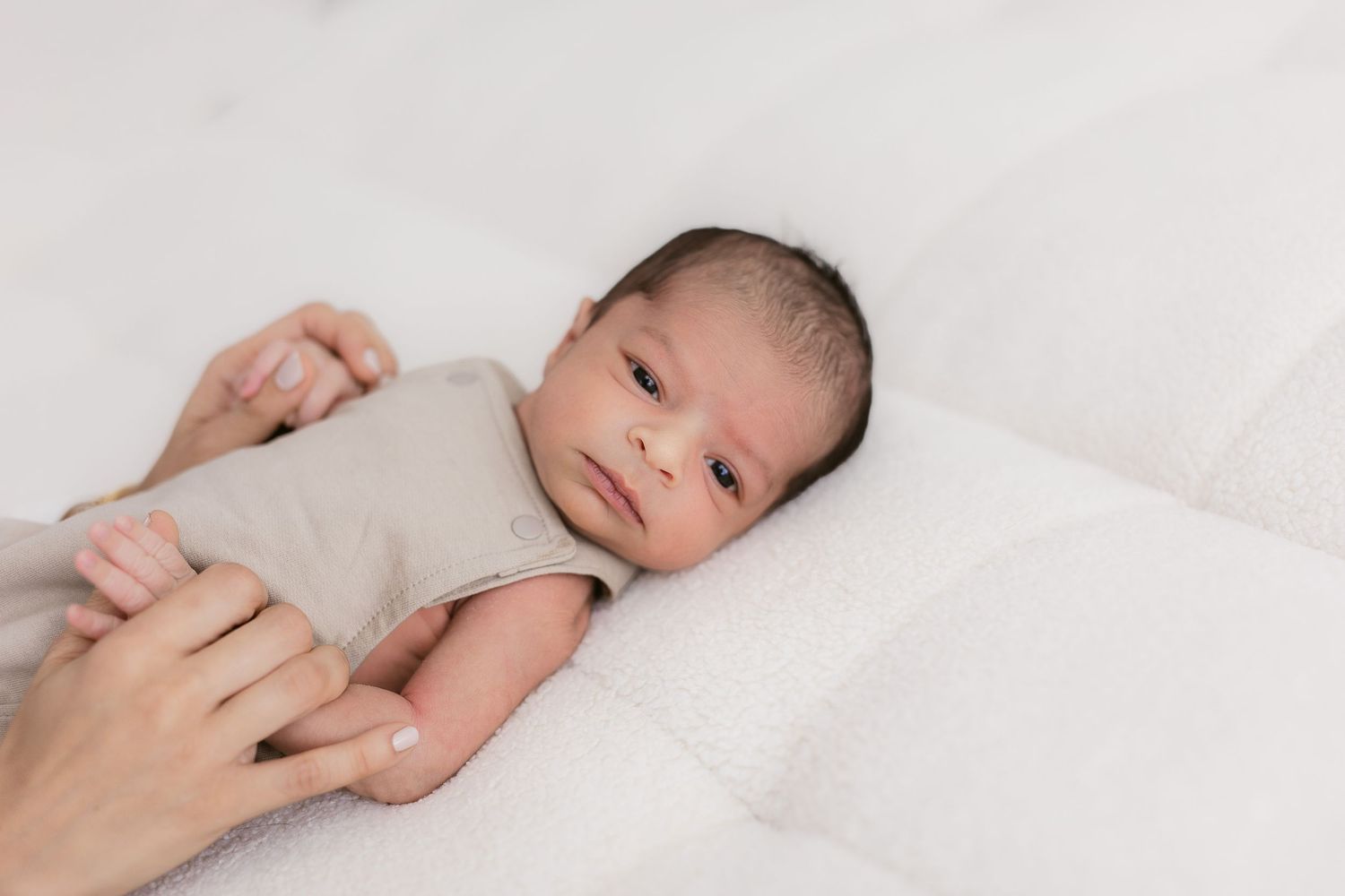 Newborn baby lying on white bedding with hands gently touching.