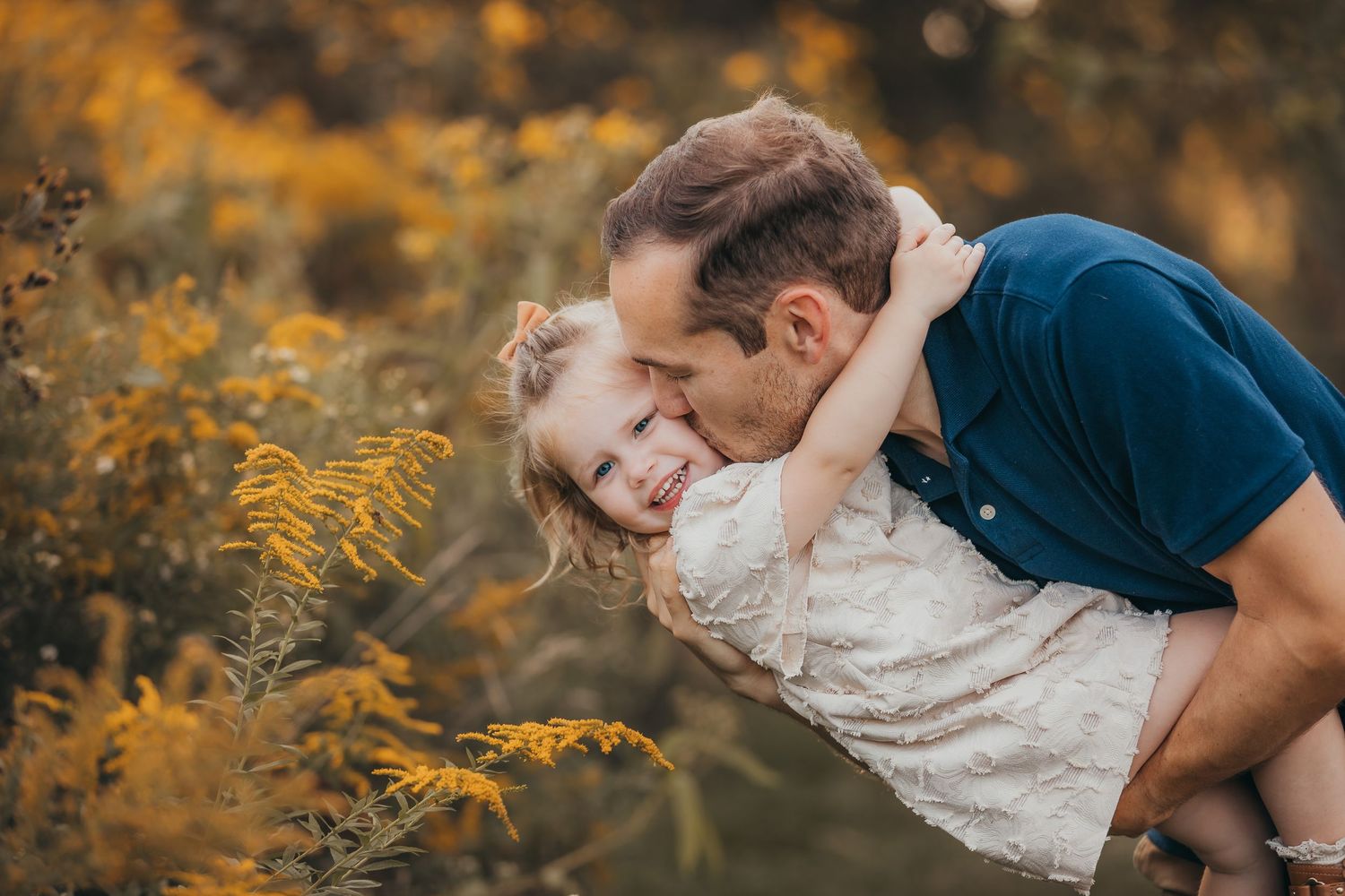 A romantic couple embraces in a golden autumn field during sunset, surrounded by warm fall foliage.