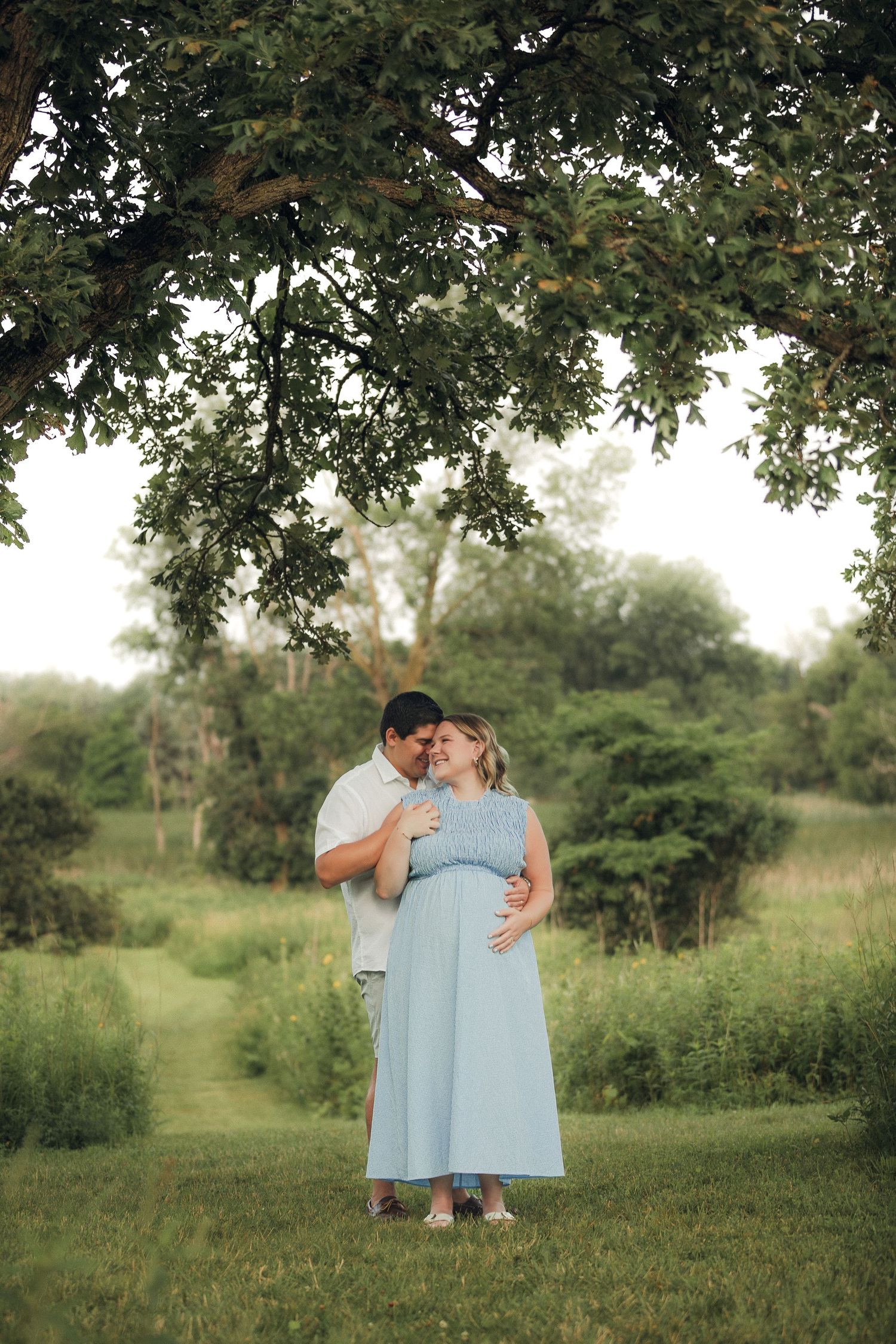 Romantic couple photos under large tree in lush summer setting.