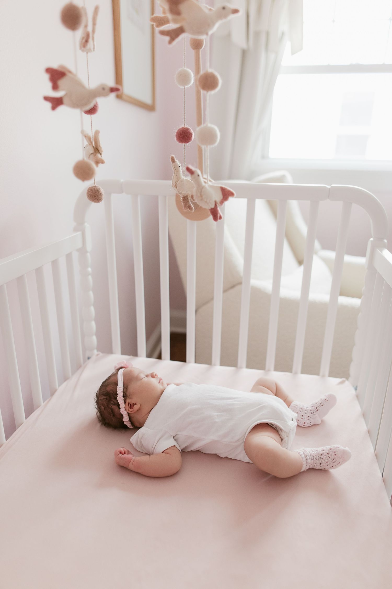 Baby resting peacefully in white crib with hanging mobile decorations.