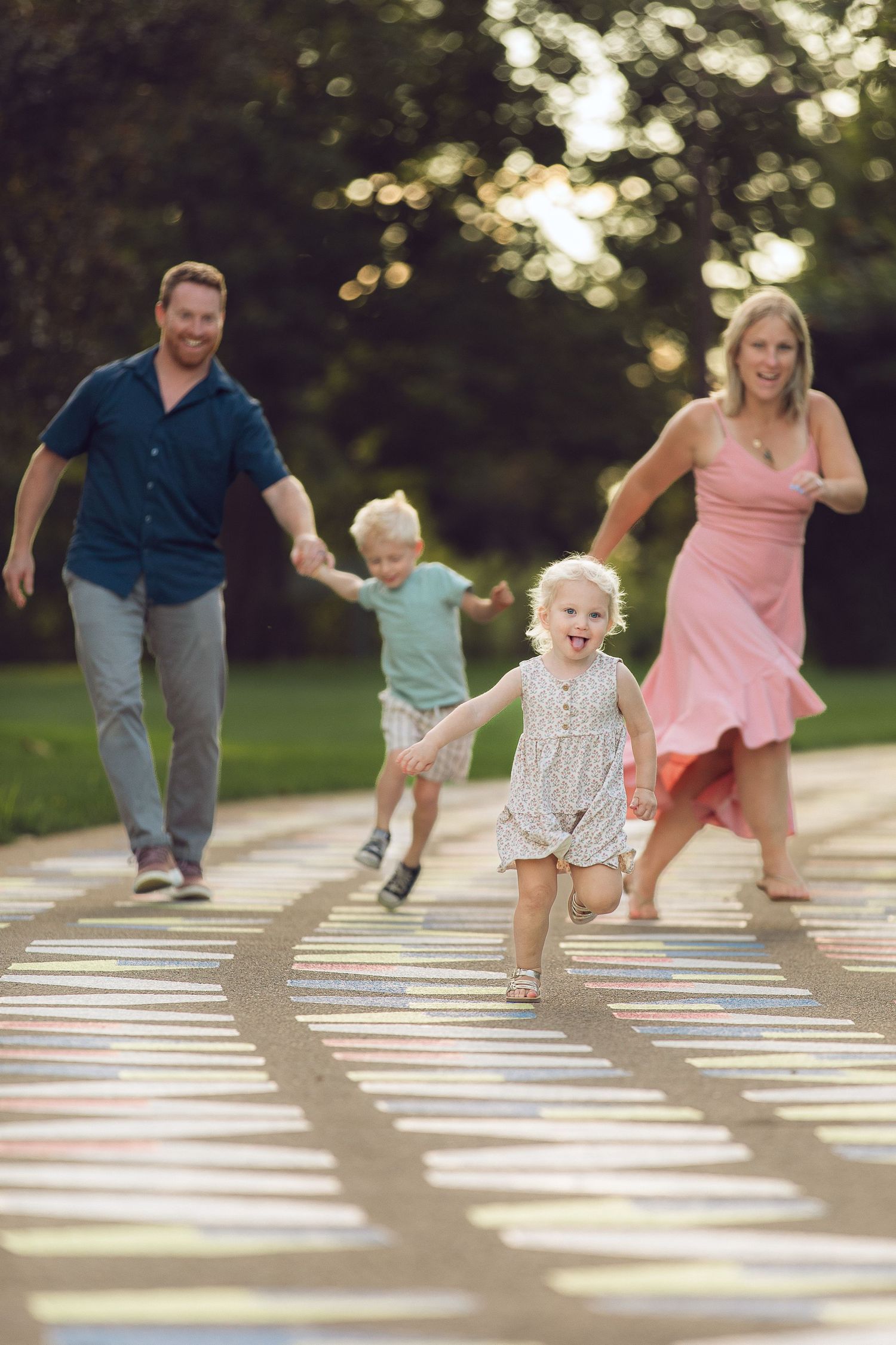 Family playing and running together on outdoor hopscotch court in park during golden hour sunset.