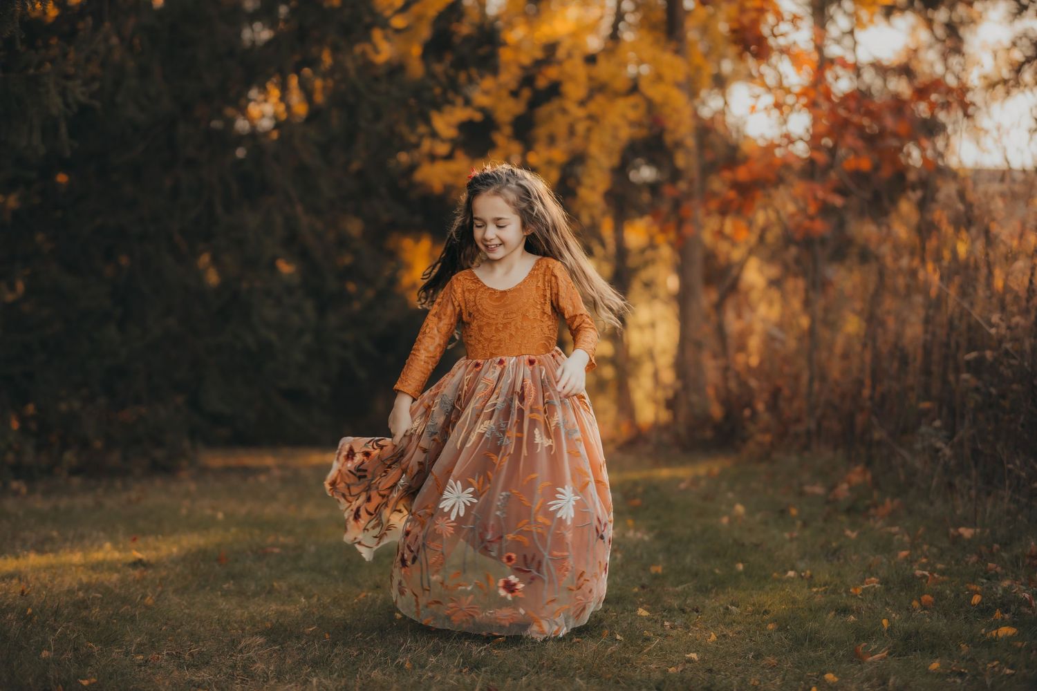 A child in a floral dress twirls in a field during golden autumn sunset light.