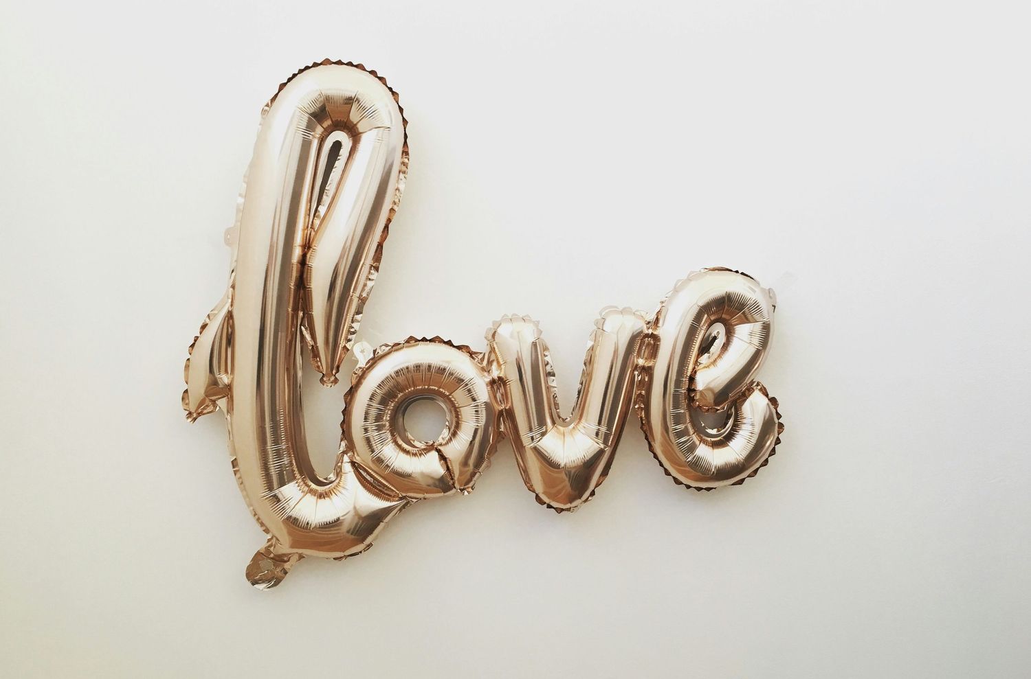 Gold metallic 'love' balloon text against white background creates romantic atmosphere.