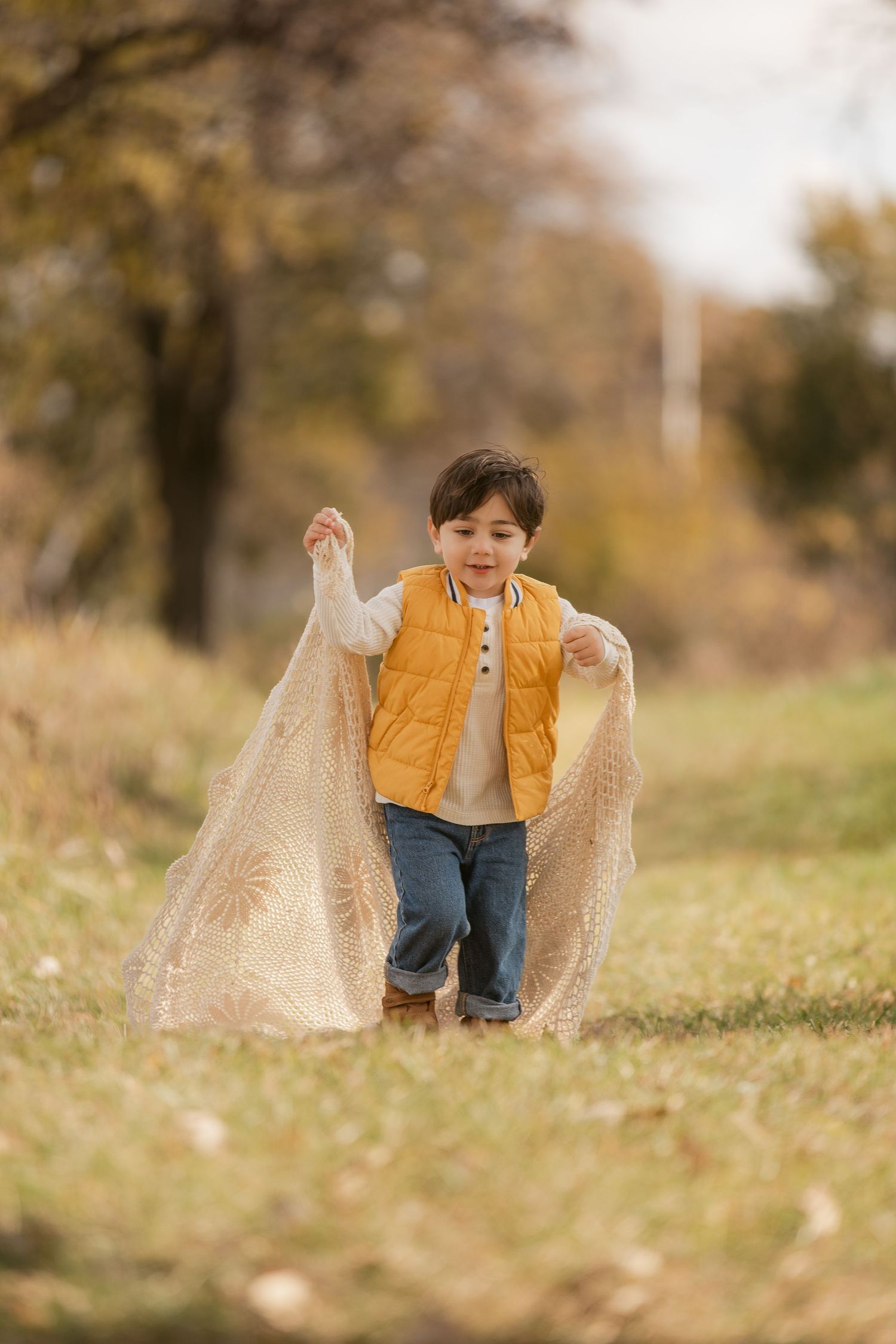 A small child plays with a beige blanket in an autumn field.