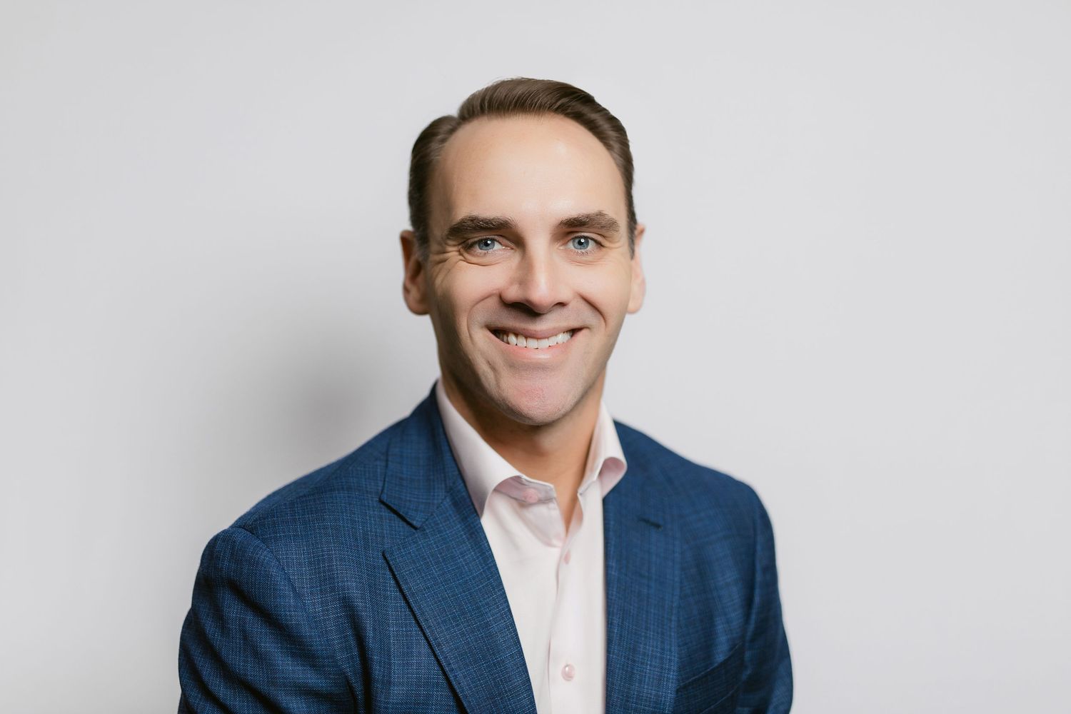 Professional headshot of person in navy suit and white shirt against grey background.