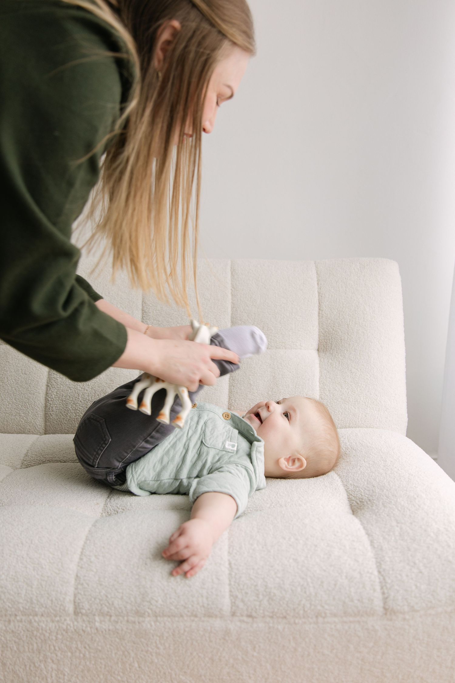 A series of photos showing a baby lying on a white couch being gently massaged by someone wearing a green sweater.