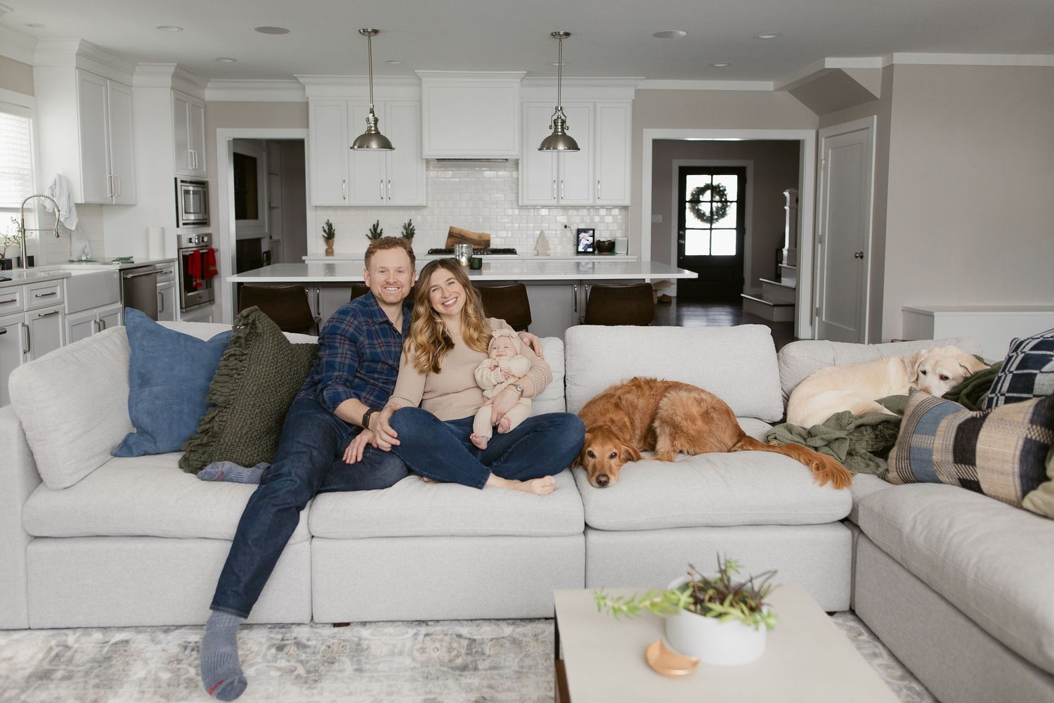 A couple relaxes on a white sectional sofa with their golden retriever in a bright, modern open-concept home.