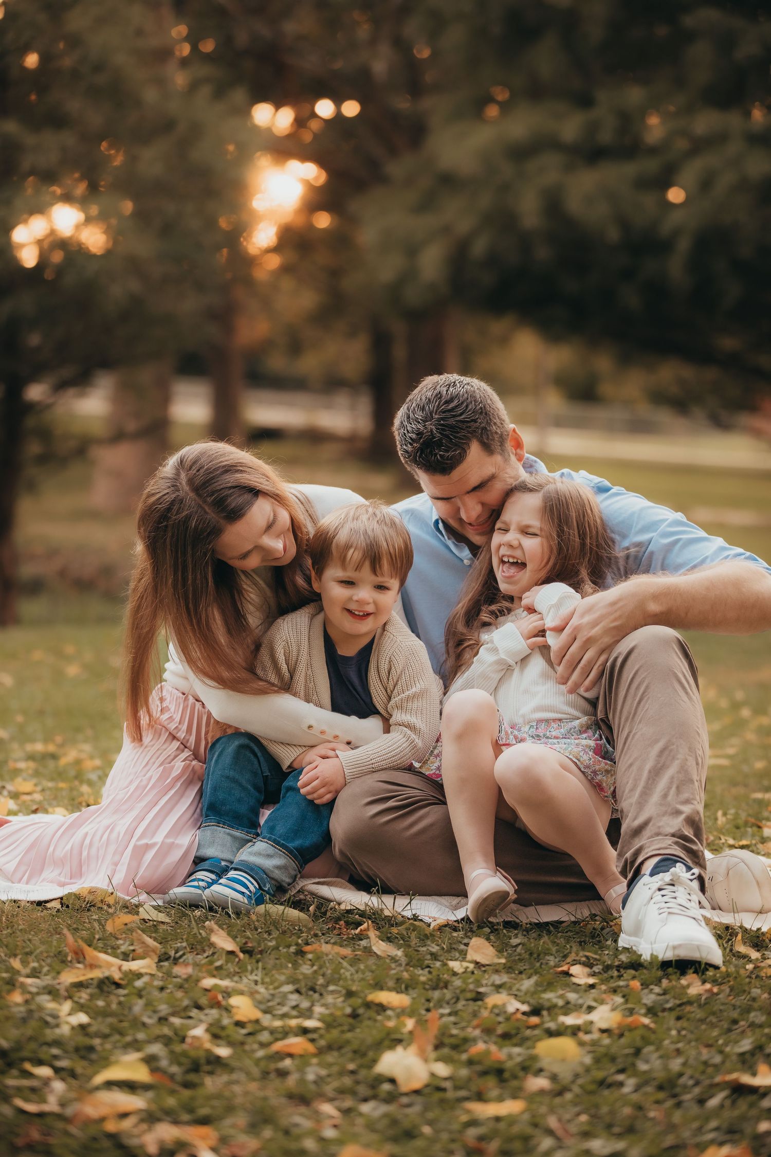 A happy family shares a joyful moment together on fallen autumn leaves at sunset in a park.