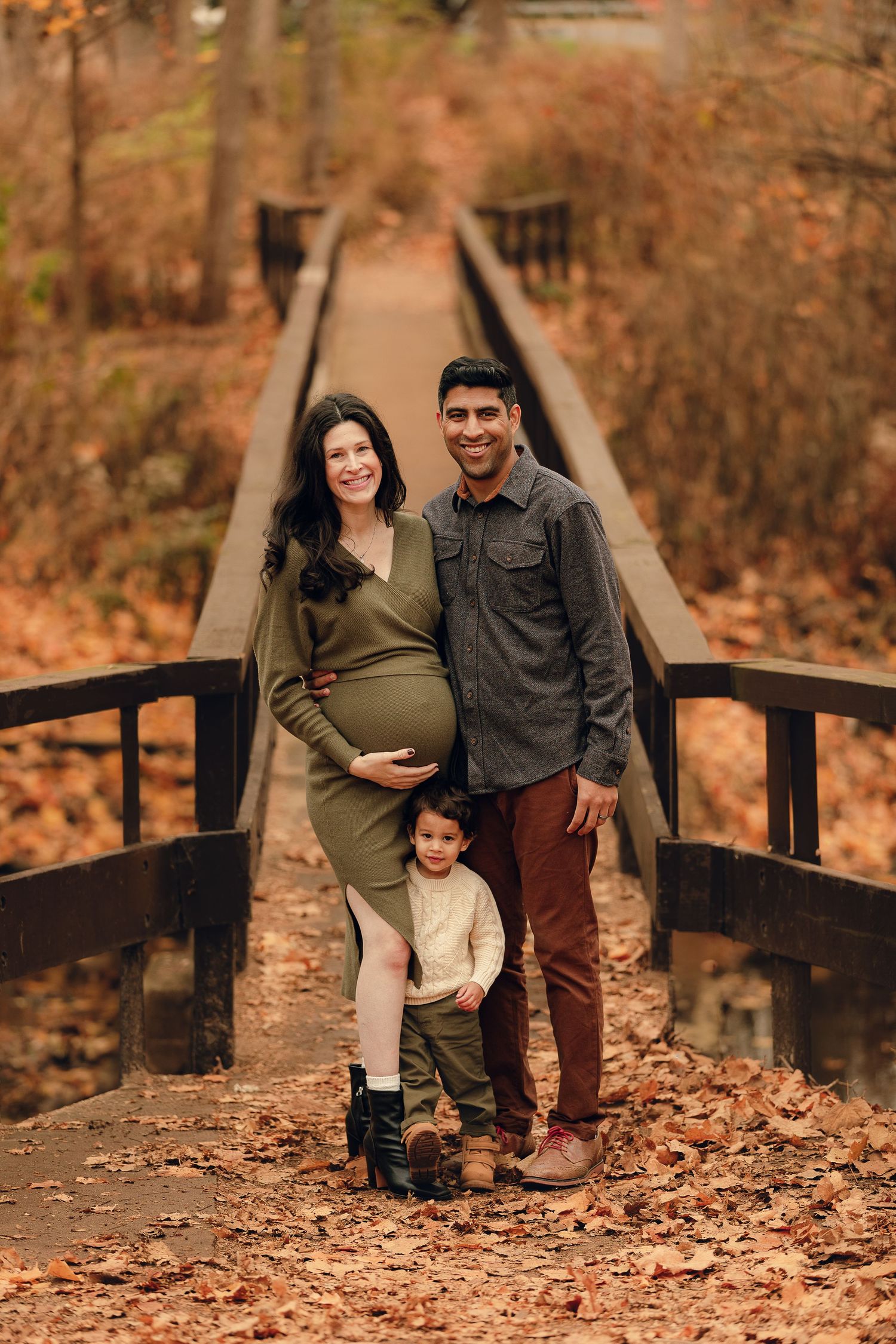 Family walking together on wooden bridge surrounded by fall foliage.