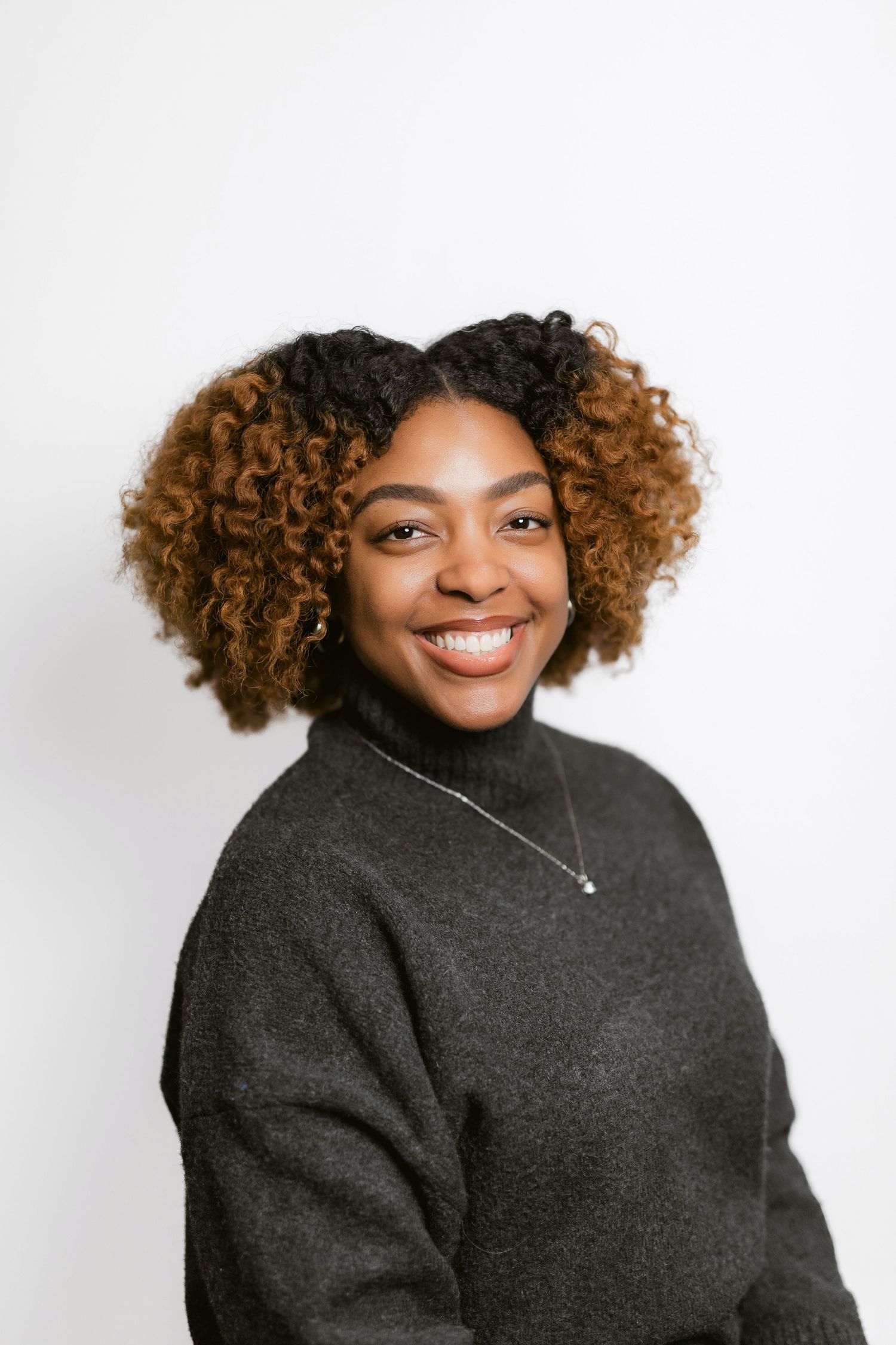 Professional portraits showing a person with curly hair wearing a dark sweater against white backdrop.
