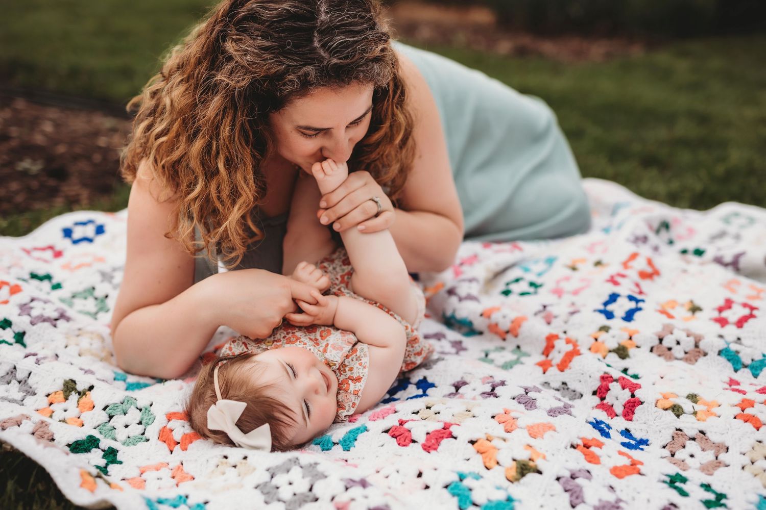 A tender moment between parent and baby lying on a colorful floral blanket in an outdoor setting.